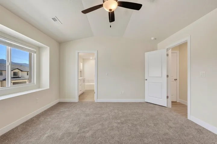 Vaulted ceiling with a ceiling fan, carpet flooring, a window offering natural light, and a white paneled door