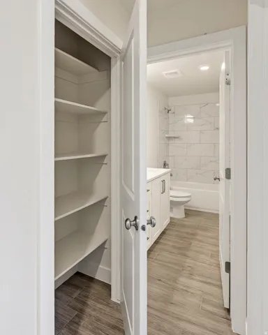 White built-in shelving, wood-finish flooring, white vanity with integrated sink, toilet, and subway tile shower surround with built-in shelf