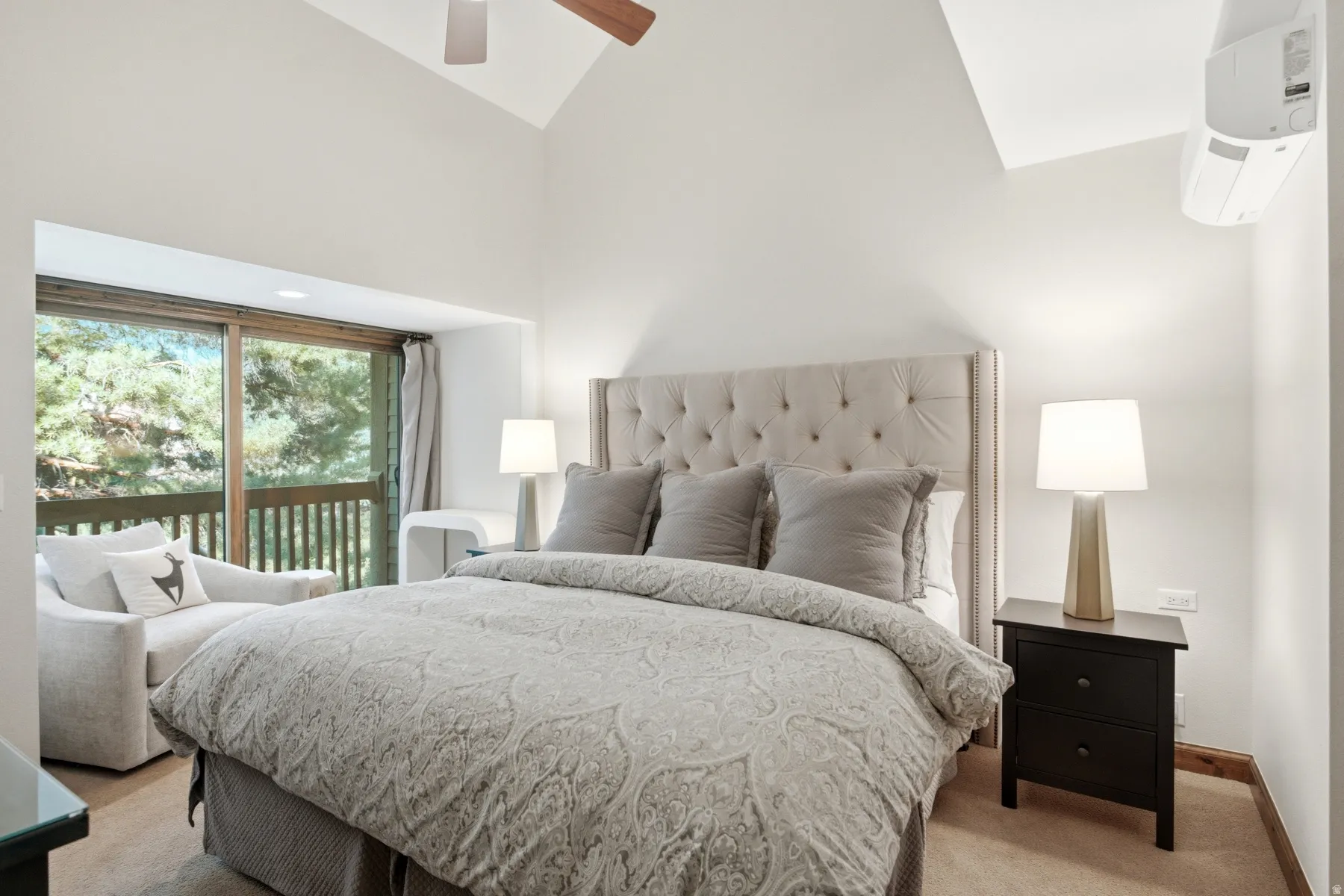 Vaulted ceiling, tufted upholstered headboard, sliding glass door, private balcony, and wall-mounted air conditioning unit