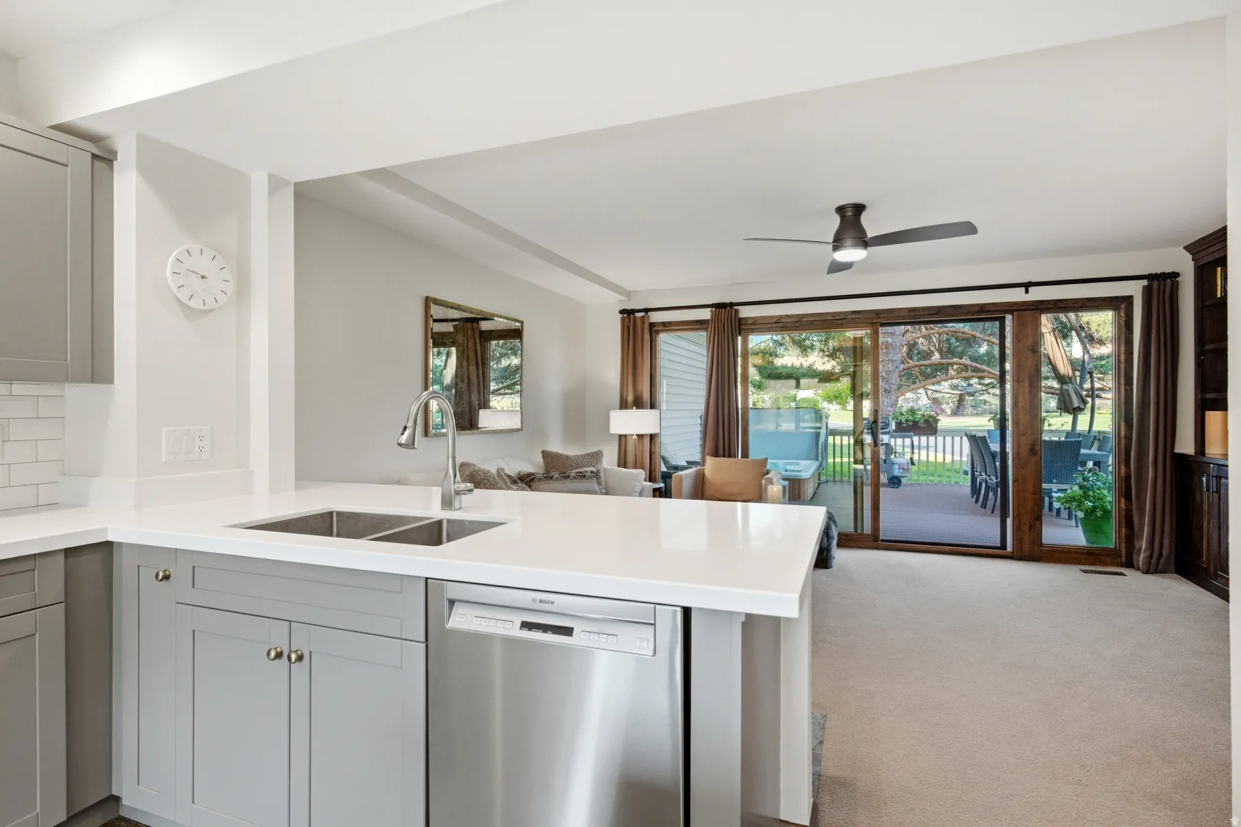 Kitchen island with a stainless steel double basin sink, gooseneck faucet, light gray cabinetry, and a built-in dishwasher