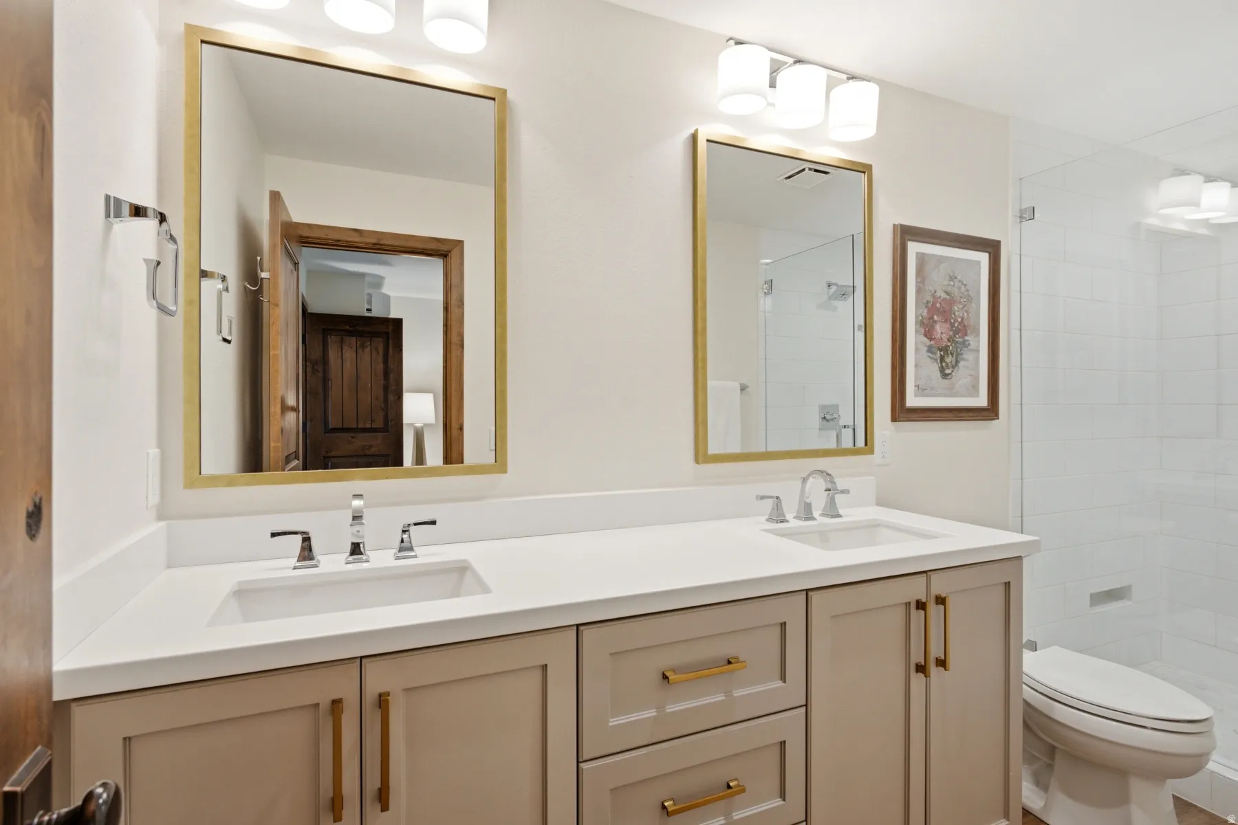 Dual vanity with integrated sinks, brushed nickel faucets, gold-framed mirrors, and under-cabinet storage