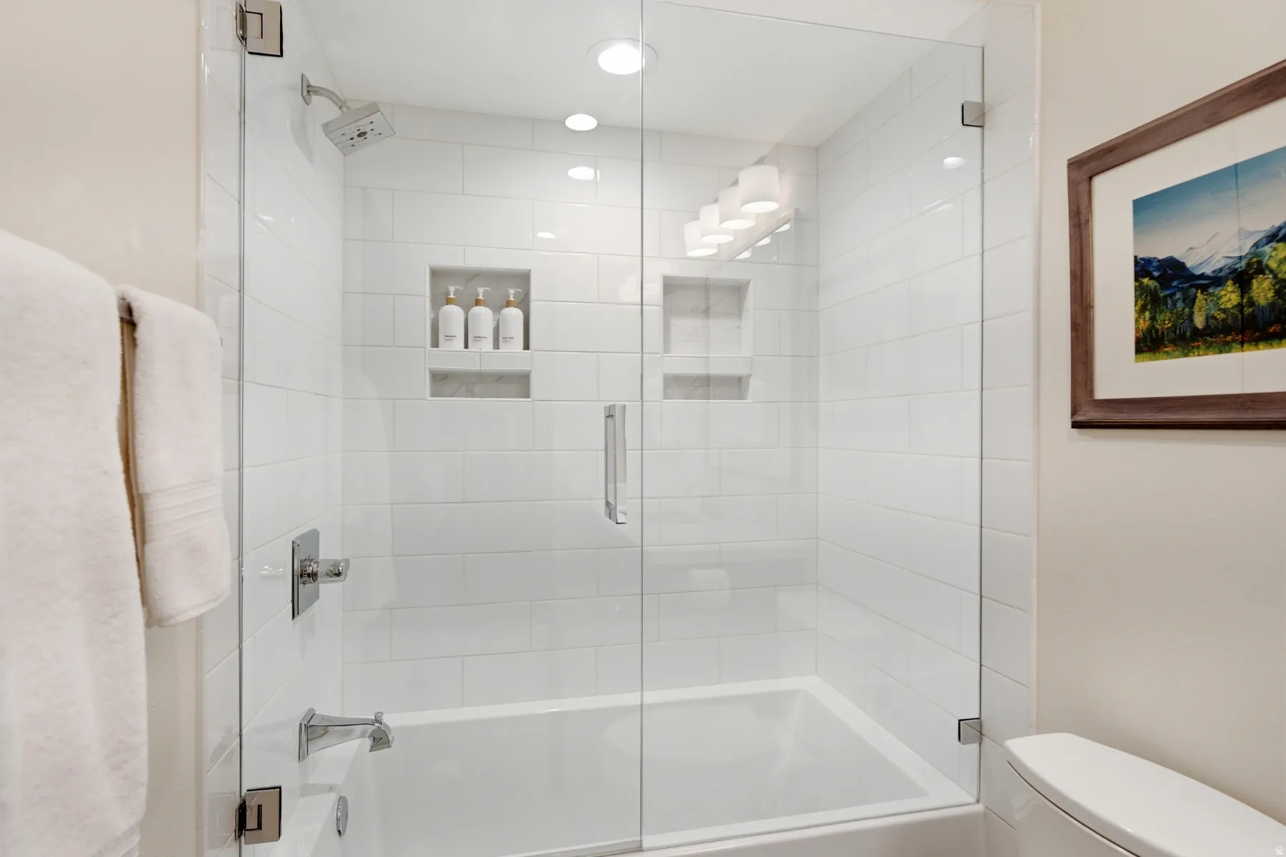 Bathtub with a glass shower enclosure, subway tile surround, recessed lighting, and integrated shower niches