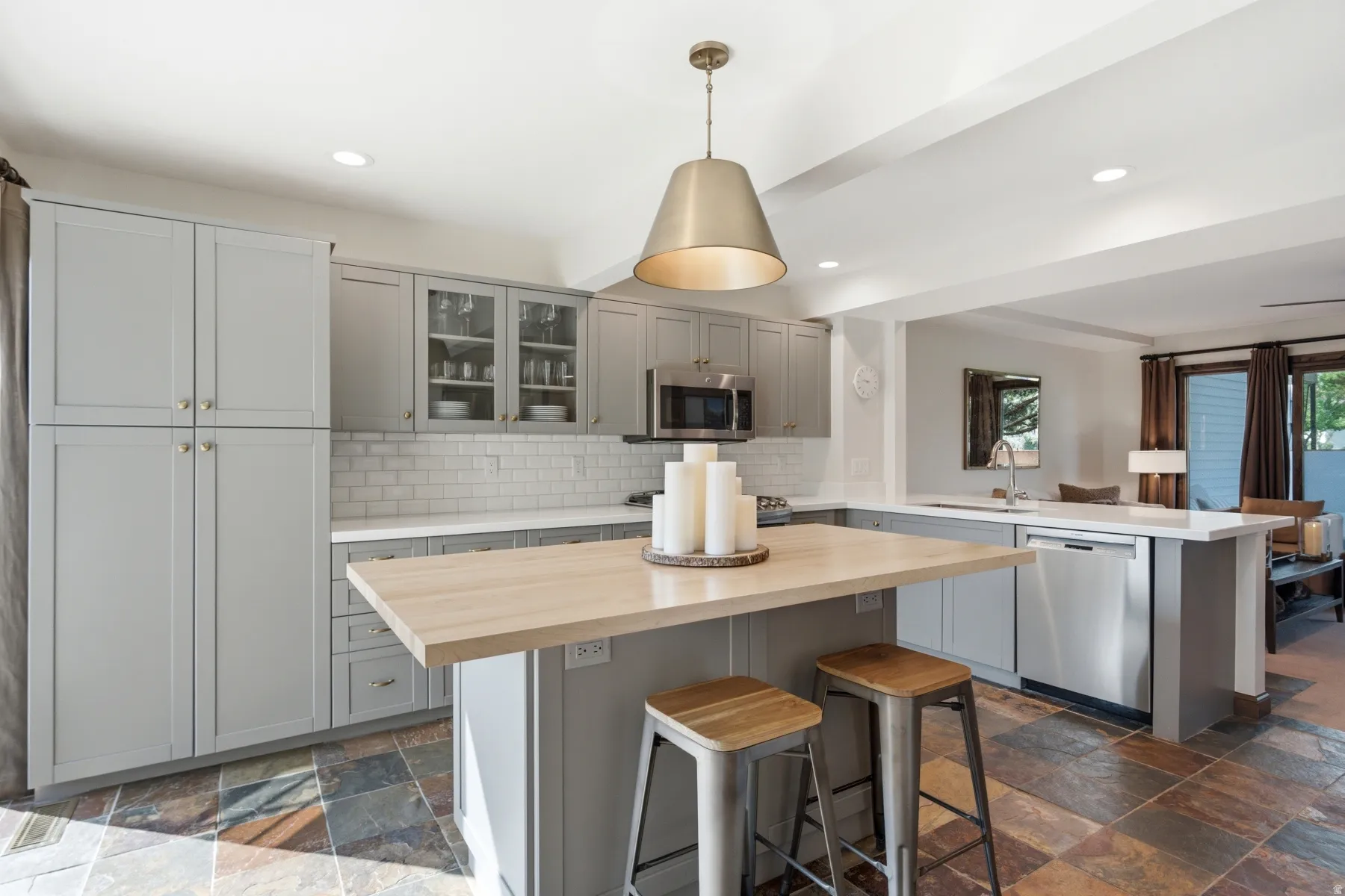 Kitchen featuring slate tile flooring, shaker-style cabinetry, a subway tile backsplash, a center island with a wood-finish countertop, and stainless steel appliances