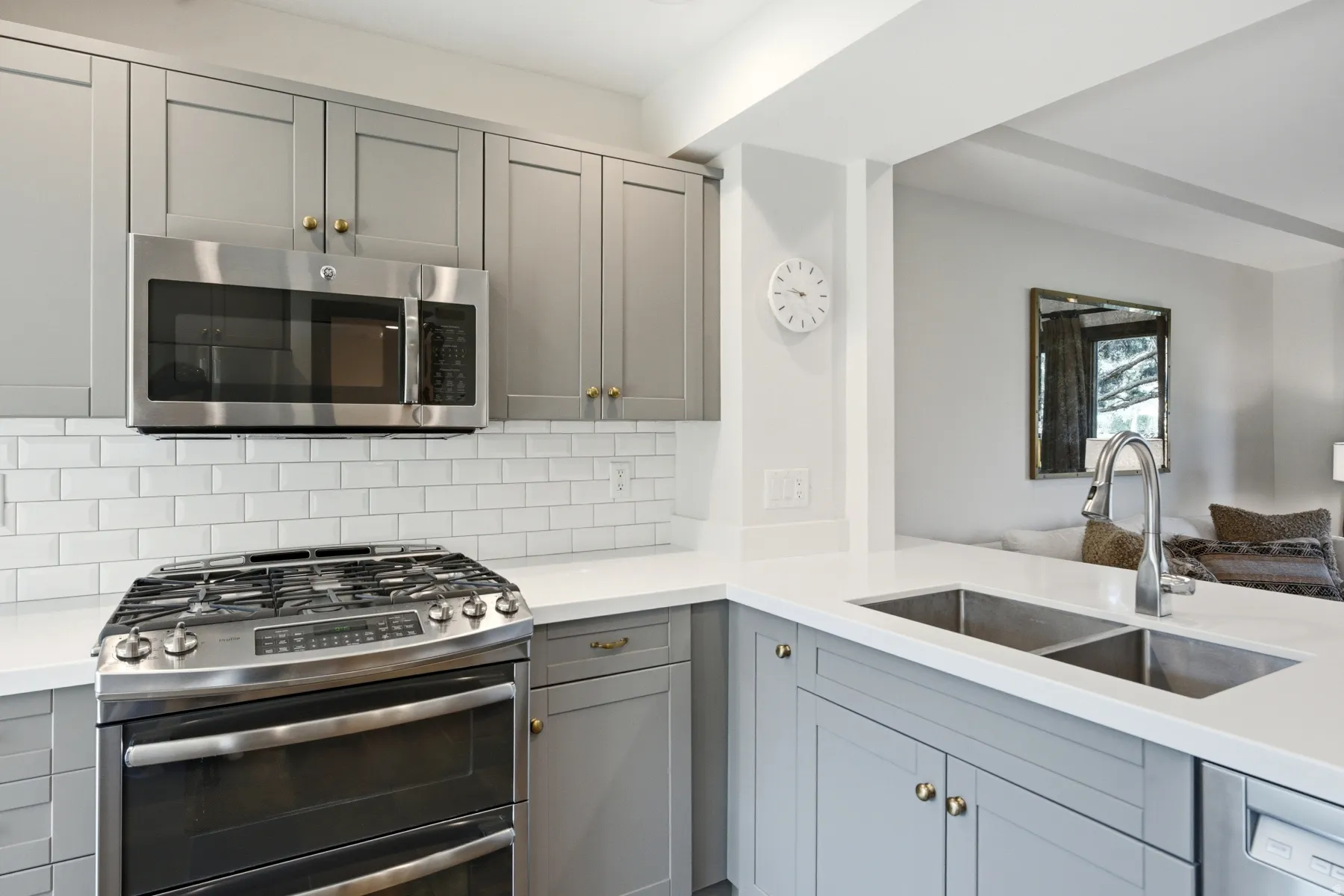 Gray shaker cabinetry, stainless steel appliances, subway tile backsplash, white countertops, and a dual basin sink