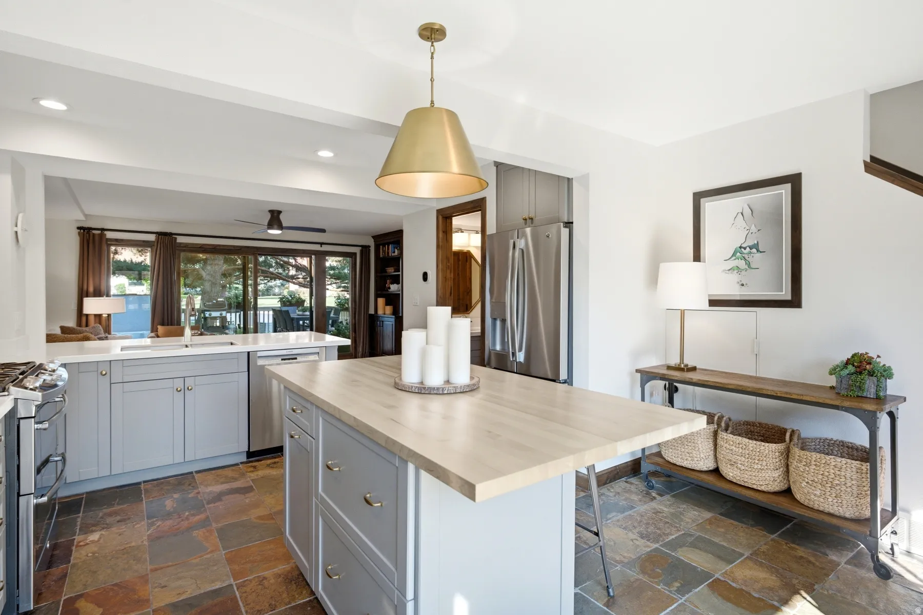 Kitchen featuring slate tile flooring, light gray cabinetry, stainless steel appliances, a center island with a wood-finish countertop, and a brass-tone pendant light fixture