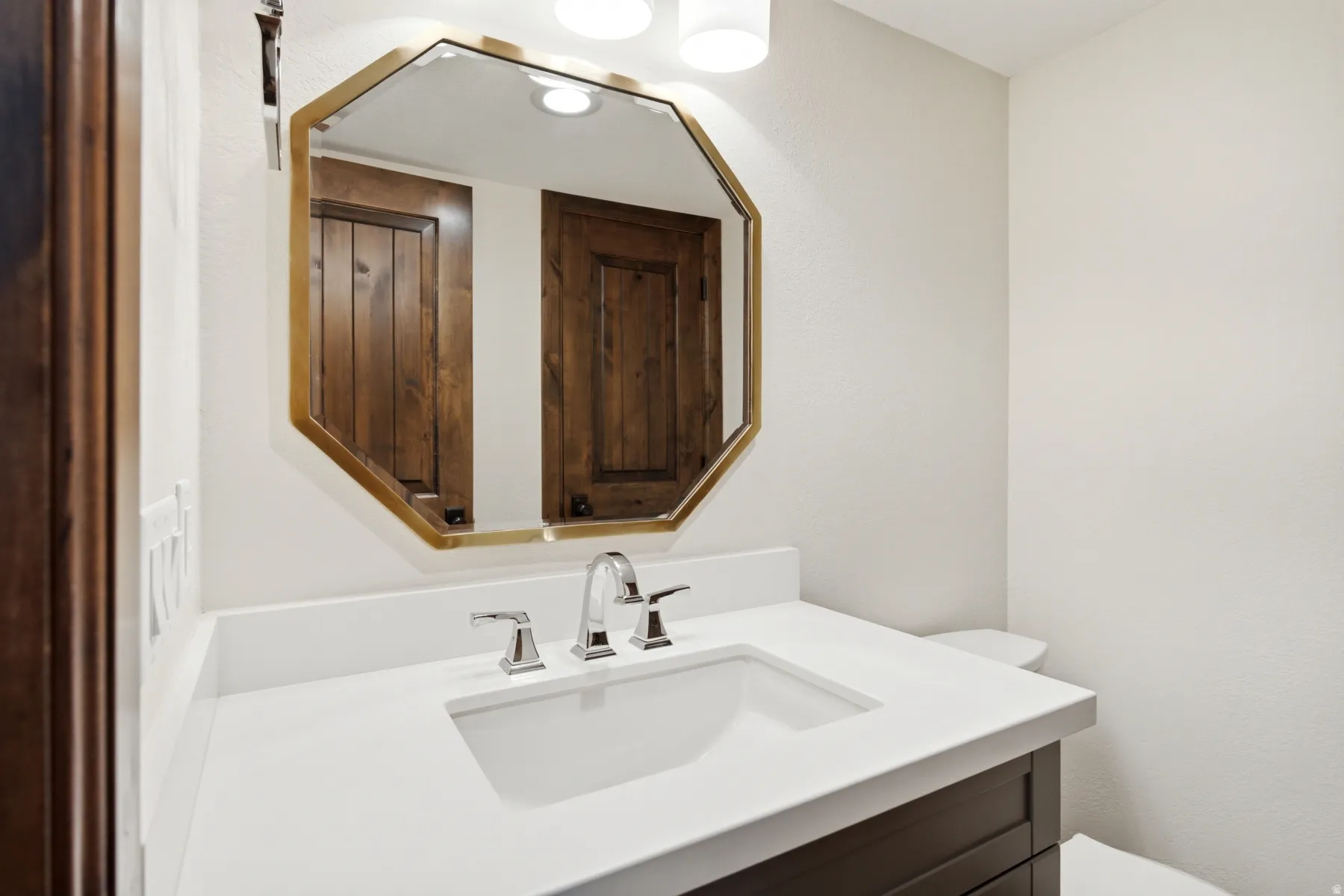 White vanity countertop with an integrated sink, polished chrome faucet, and a hexagonal framed mirror