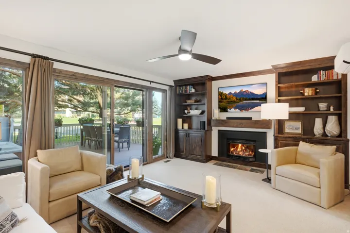 Built-in shelving, wood mantel fireplace, recessed lighting, ceiling fan, and sliding glass doors to outdoor decking