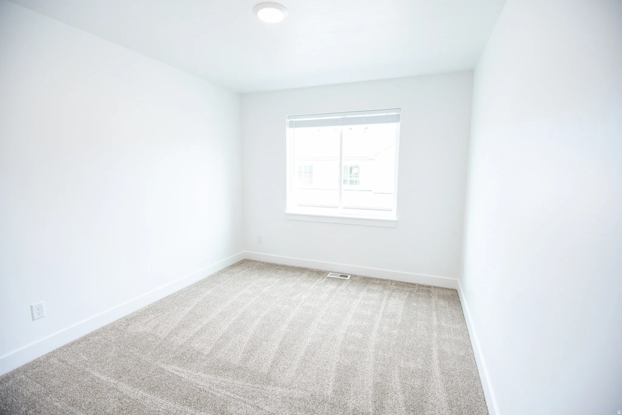 Recessed lighting fixture, light gray carpeting, white walls, and a single window