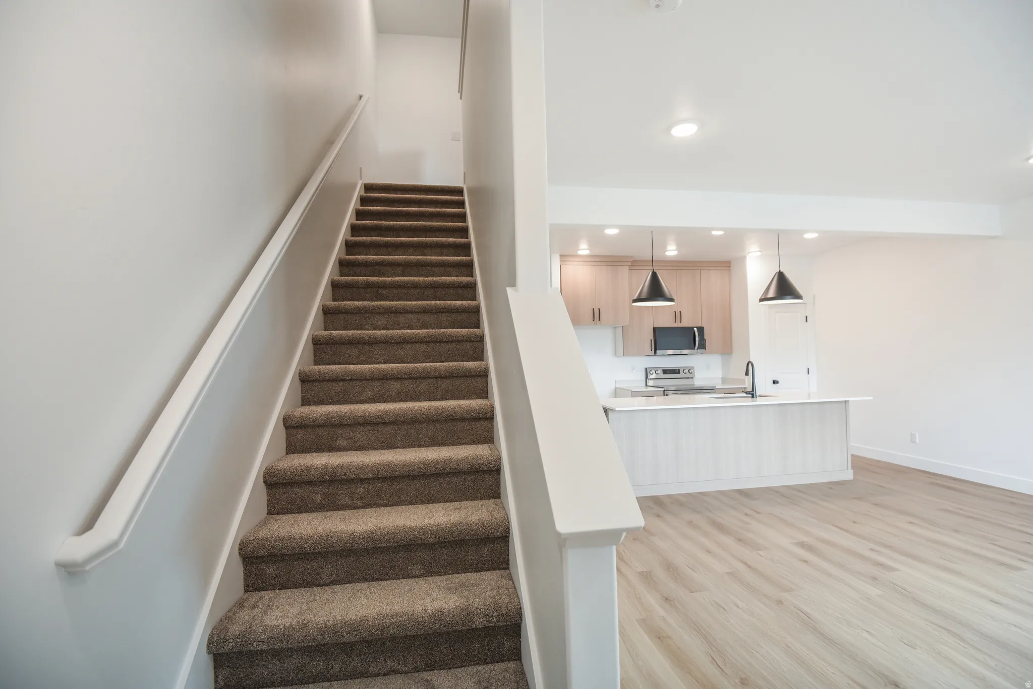 Carpeted staircase with white handrail, recessed lighting, wood-finish flooring, light wood cabinetry, and a kitchen island with pendant lighting