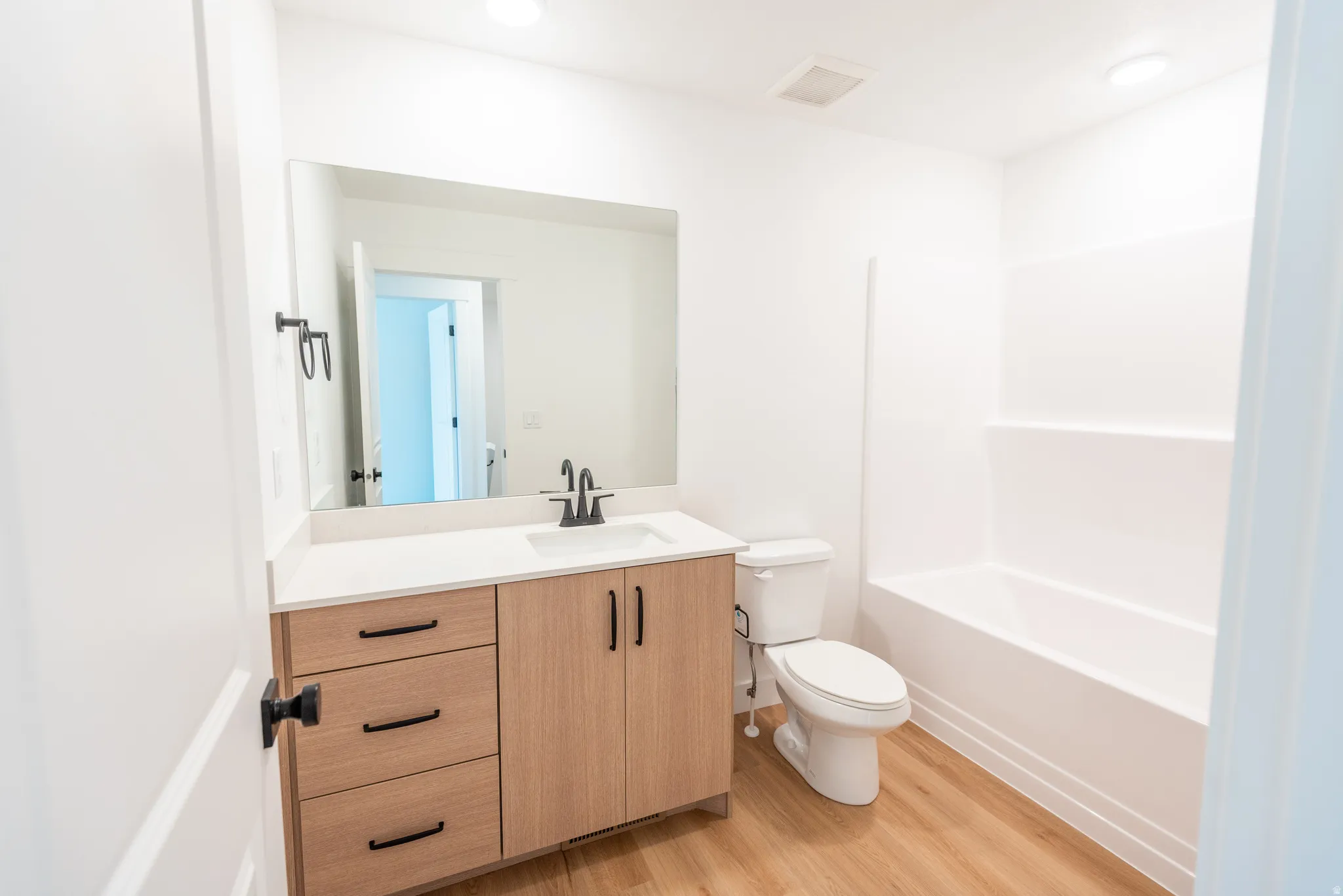 Bathroom featuring a wood-finish vanity with a light-toned countertop, integrated sink, and matte black fixtures