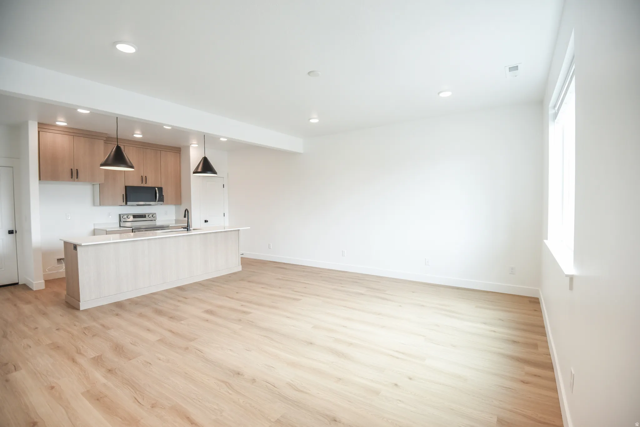 Open-concept living space with wood-finish flooring, recessed lighting, and a window