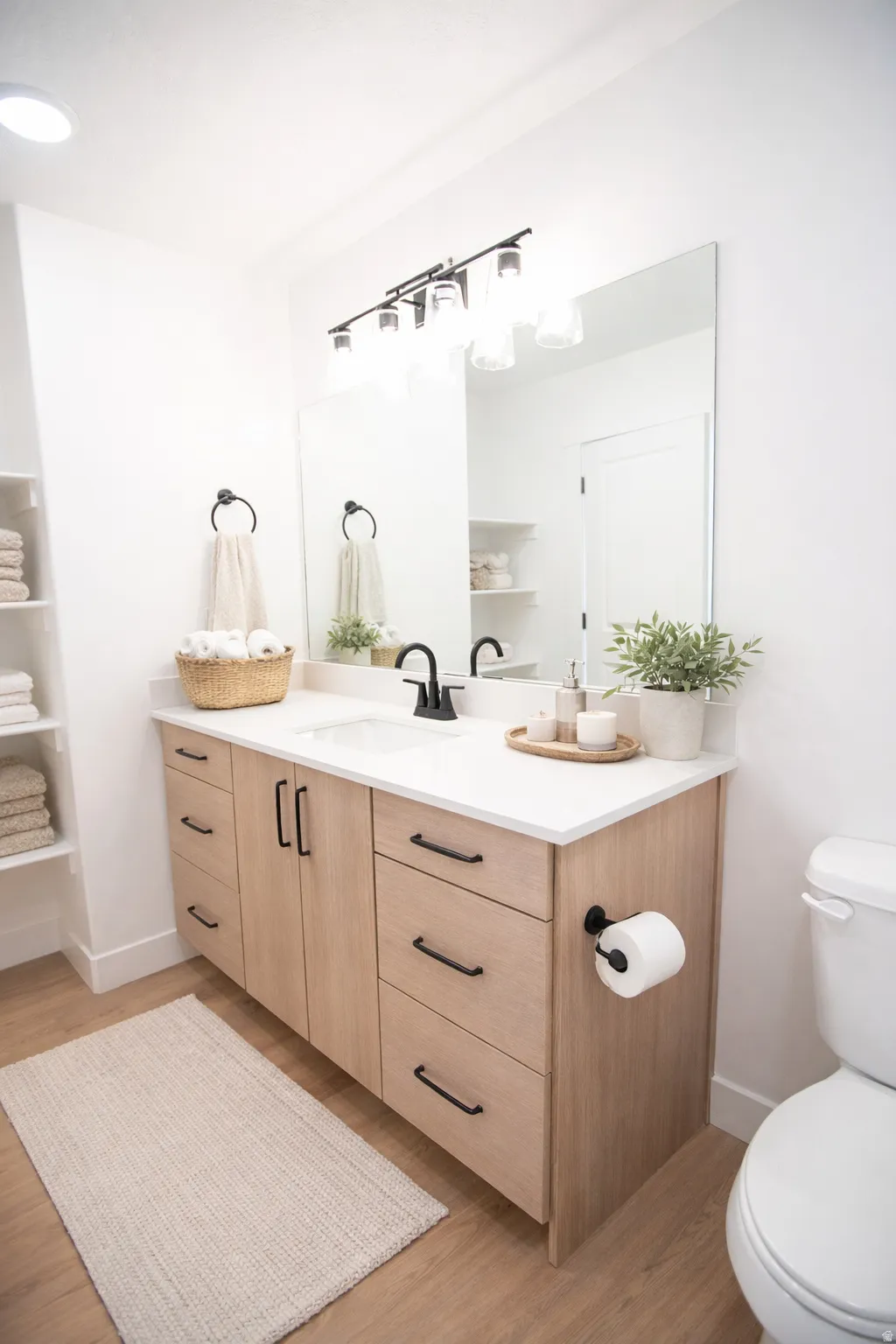 Wood-finish vanity with ample storage and matte black hardware, white countertop with integrated sink, black wall-mounted faucet, and wood-finish flooring
