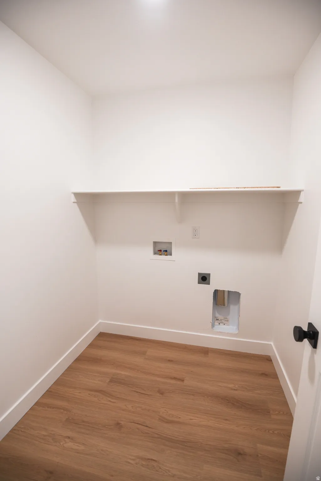 Utility space featuring wood-finish flooring, a wall-mounted shelf, and appliance hookups