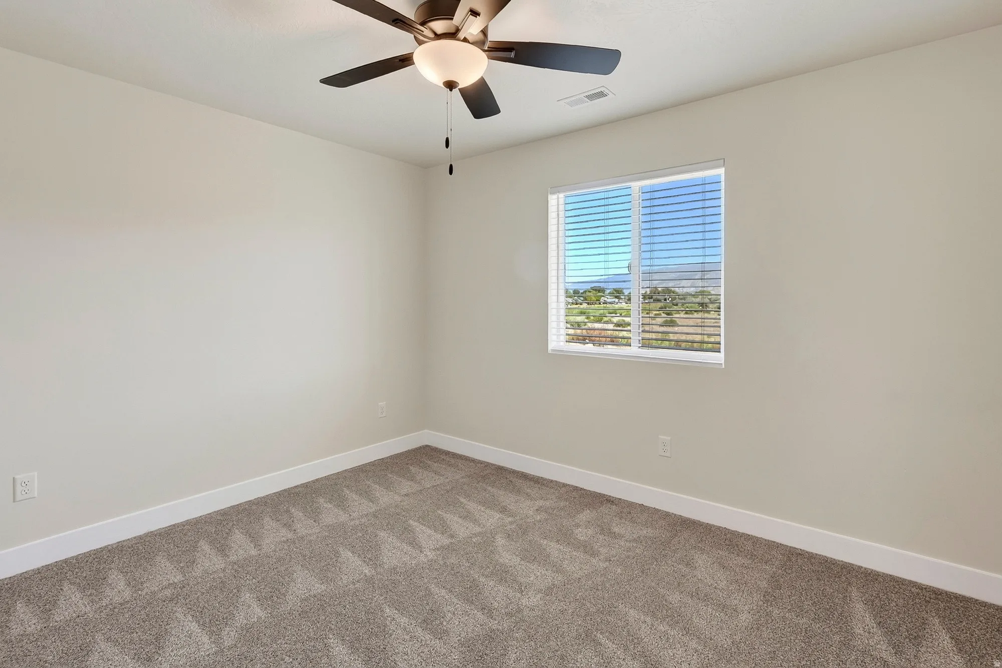Neutral wall paint, patterned carpeting, ceiling fan with integrated lighting, and window with blinds