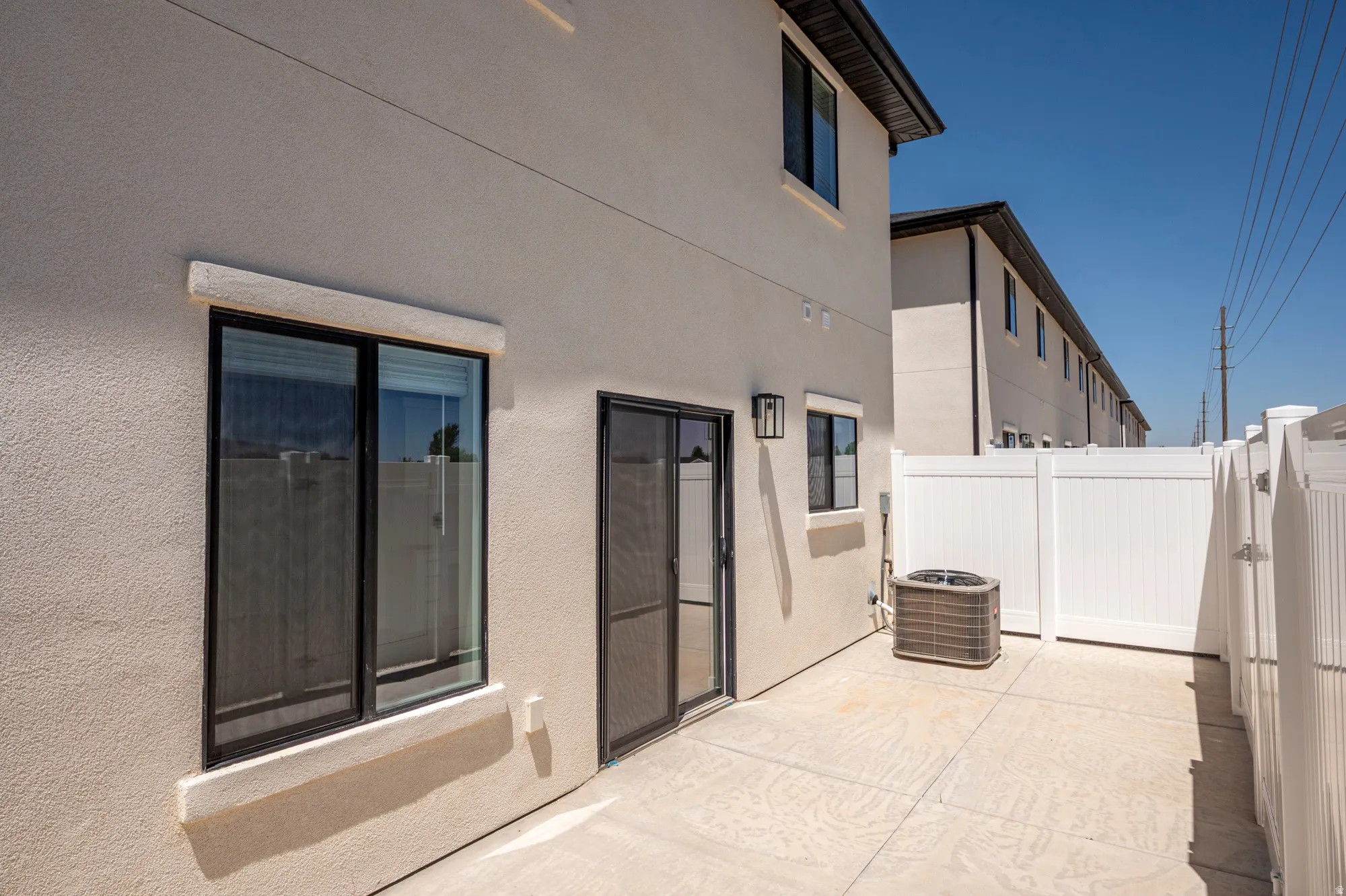 Exterior featuring stucco siding, sliding glass patio door, exterior lighting, window with dark trim, and a white privacy fence