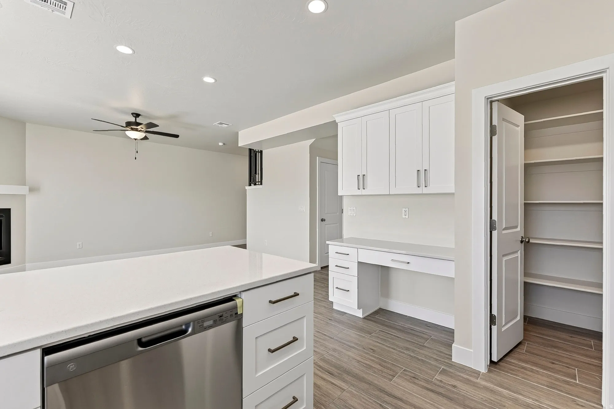 White shaker cabinetry with dark hardware, built-in desk area, recessed lighting, stainless steel appliance, and wood-finish flooring