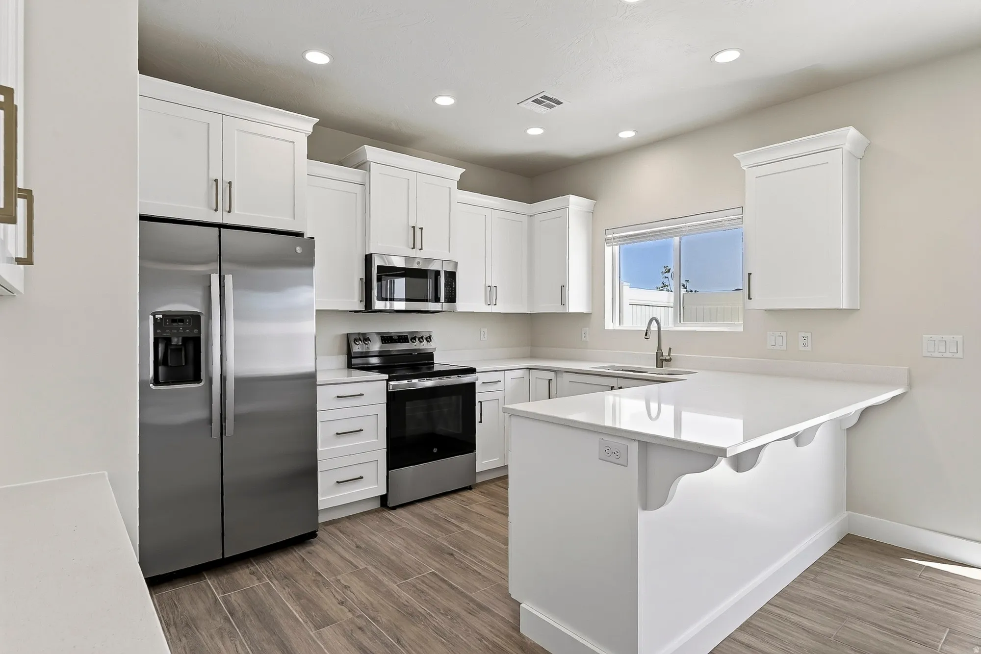 White shaker cabinetry, stainless steel appliances, white countertops, wood-finish flooring, and an eat-at island