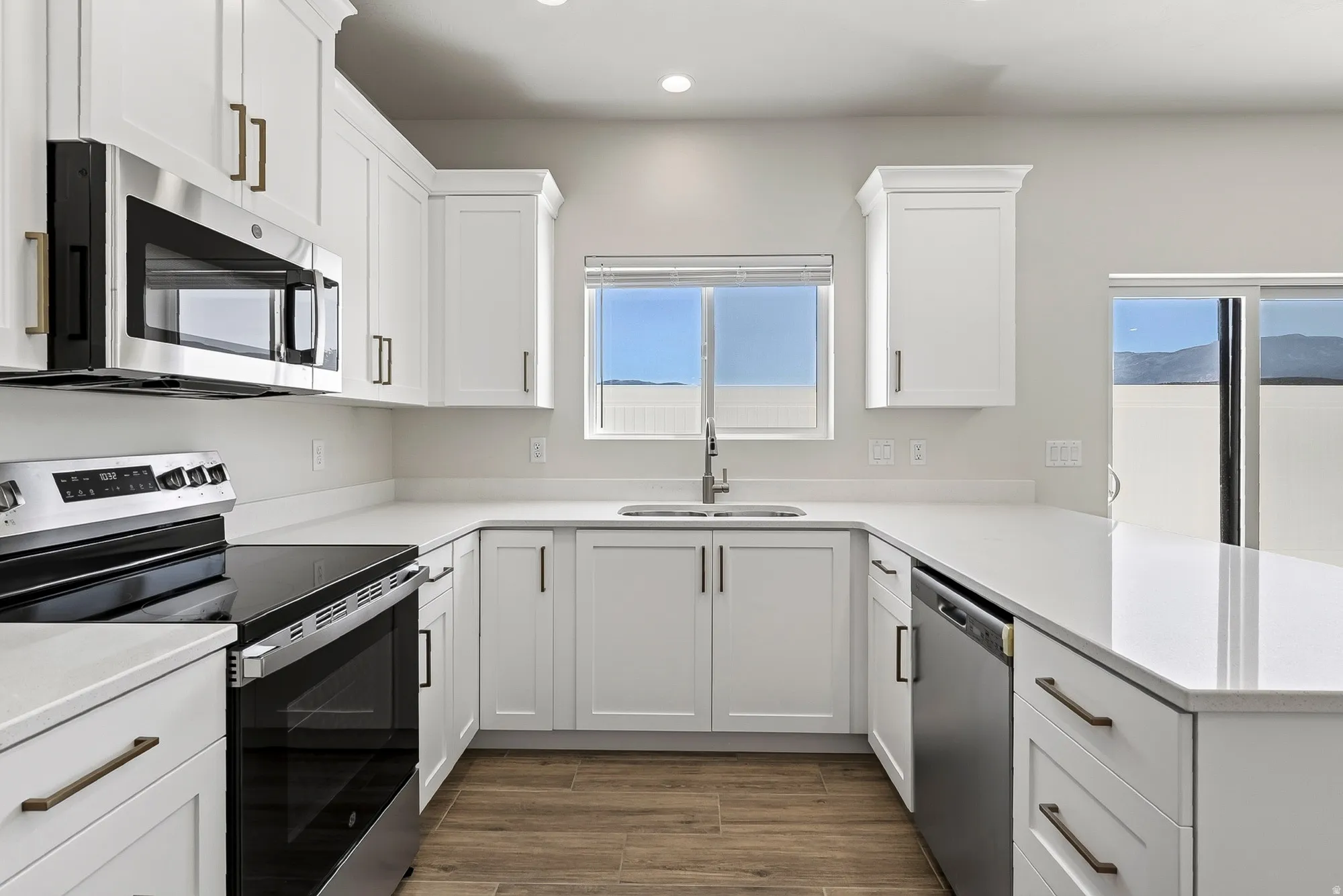 U-shaped kitchen with white cabinetry, stainless steel appliances, light-toned countertops, and wood-finish flooring