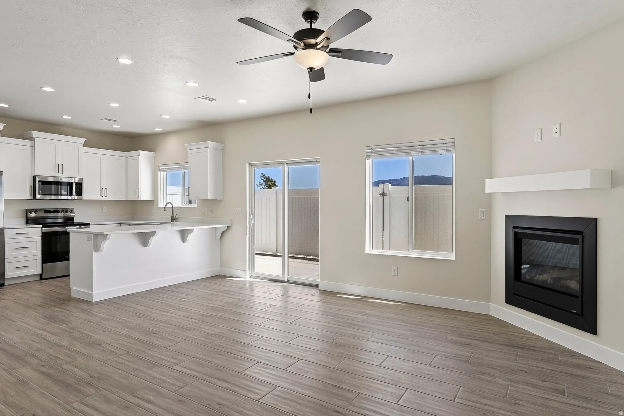 Open-concept living space featuring wood-finish flooring, a contemporary fireplace, and a ceiling fan