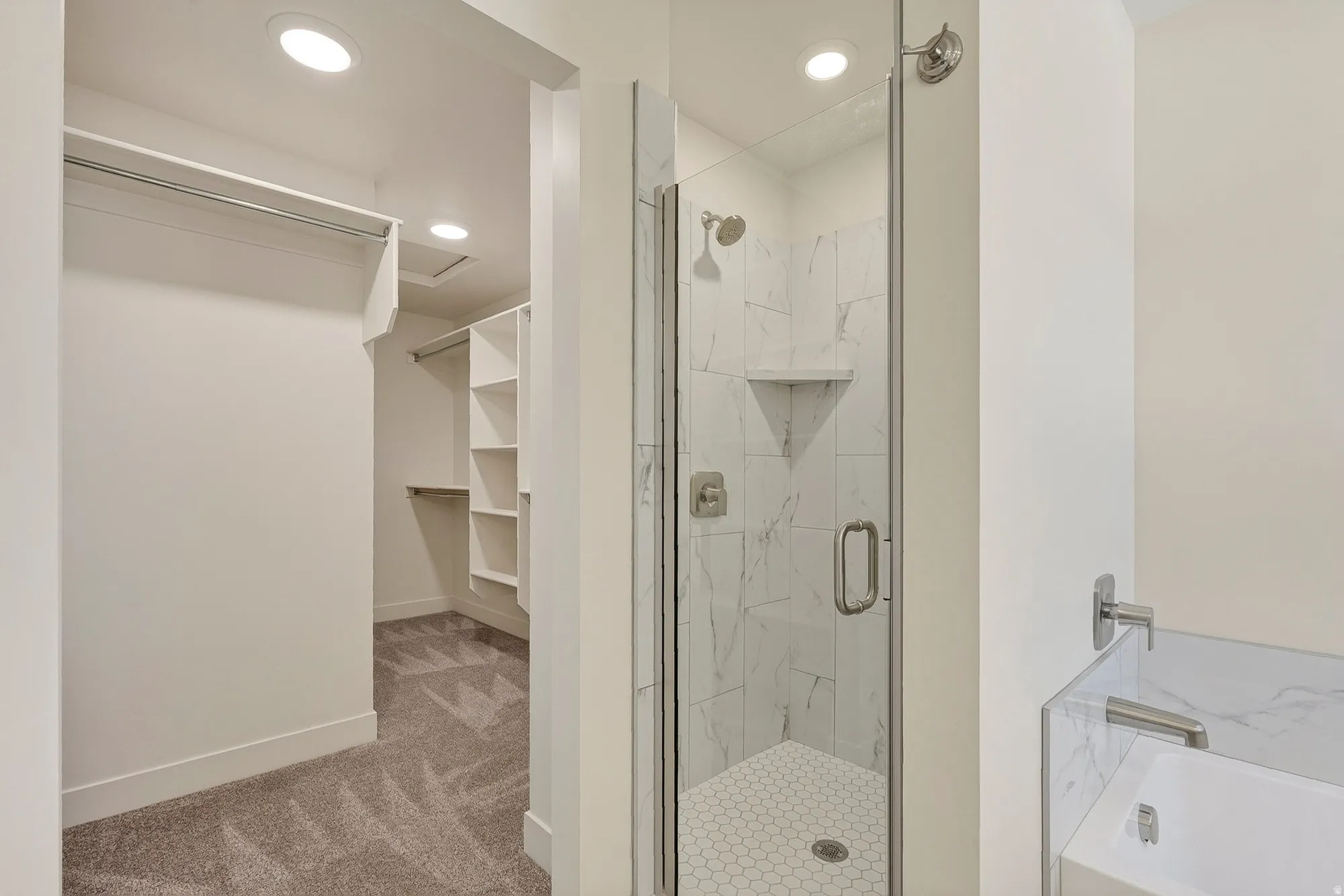 Walk-in closet with built-in shelving, glass-enclosed shower with marble-look tile, rainfall showerhead, and a built-in tub with marble-look surround