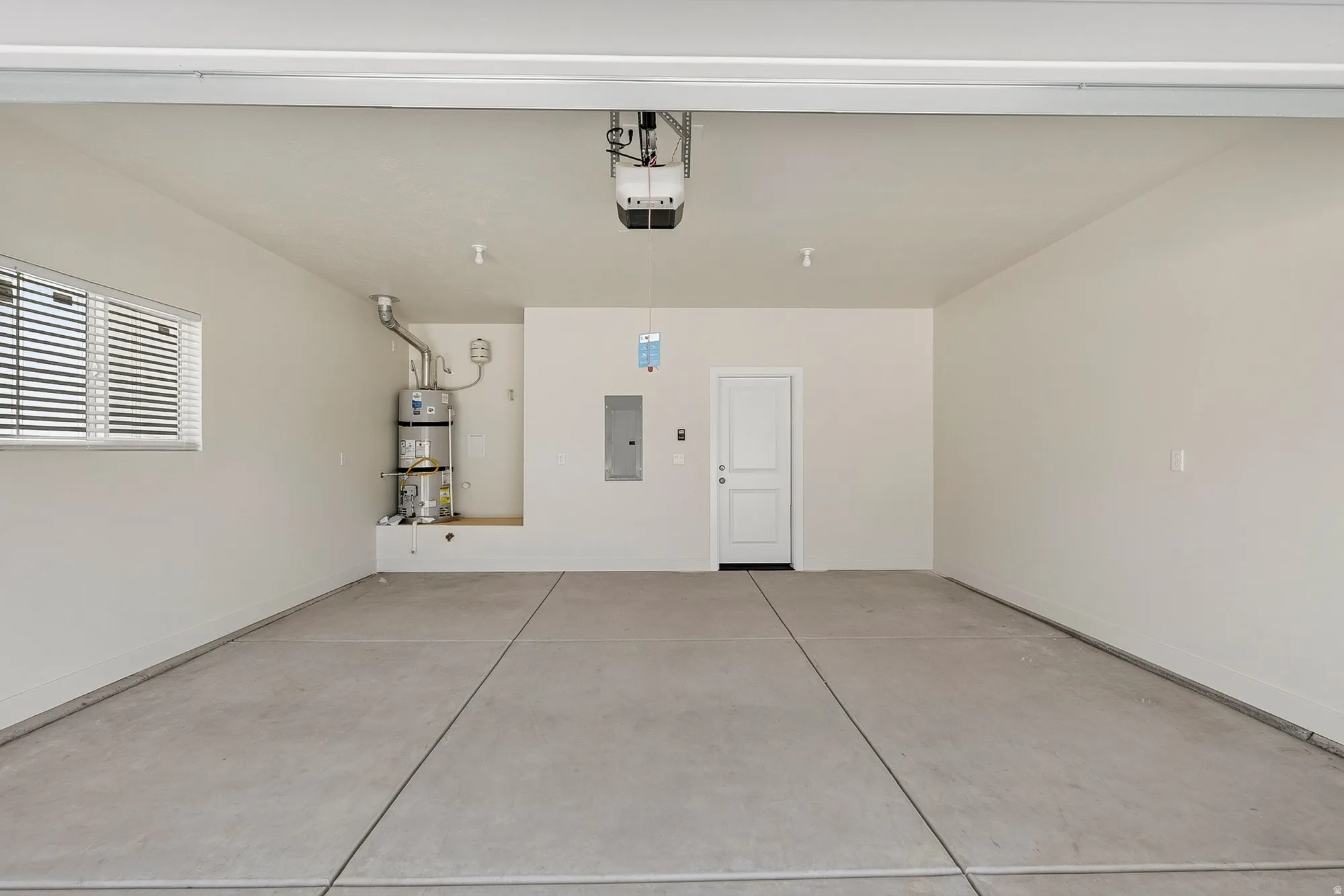 Spacious garage featuring a finished concrete floor, window with horizontal blinds, and a built-in water heater