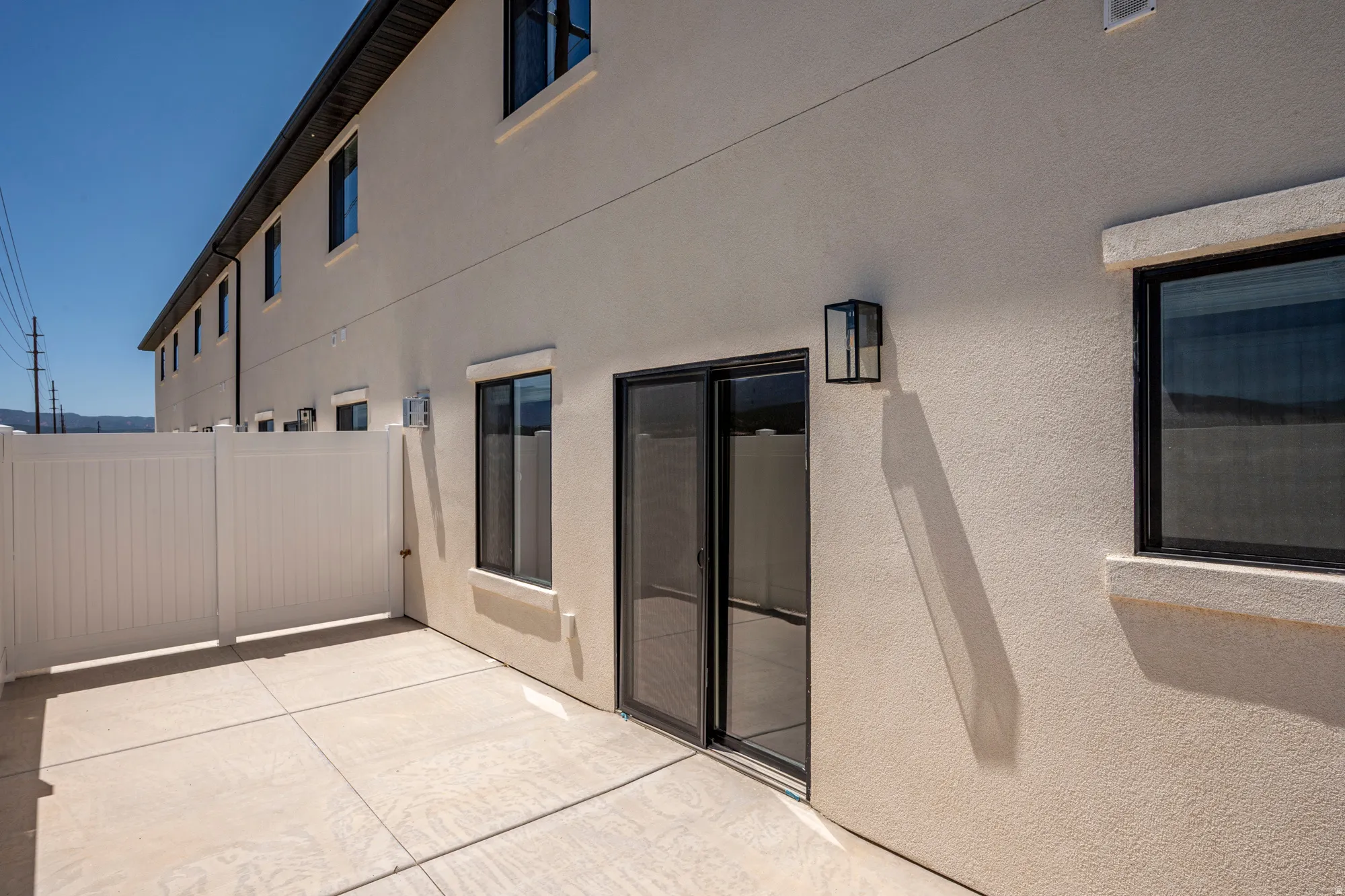 Private patio area with concrete flooring, white vinyl fencing, and a modern exterior light fixture