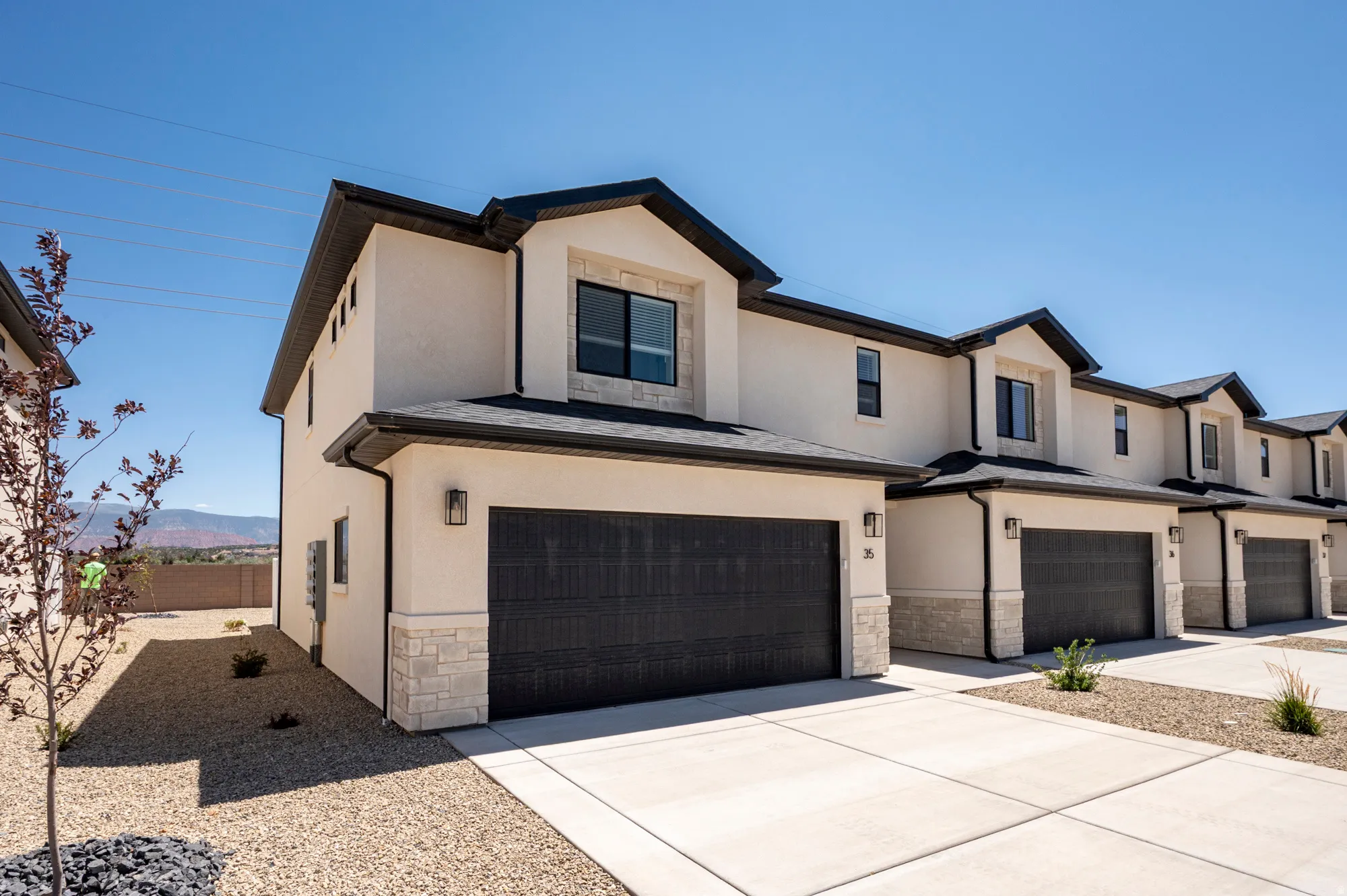 Stucco exterior with stone accents, black garage doors, and a paved driveway