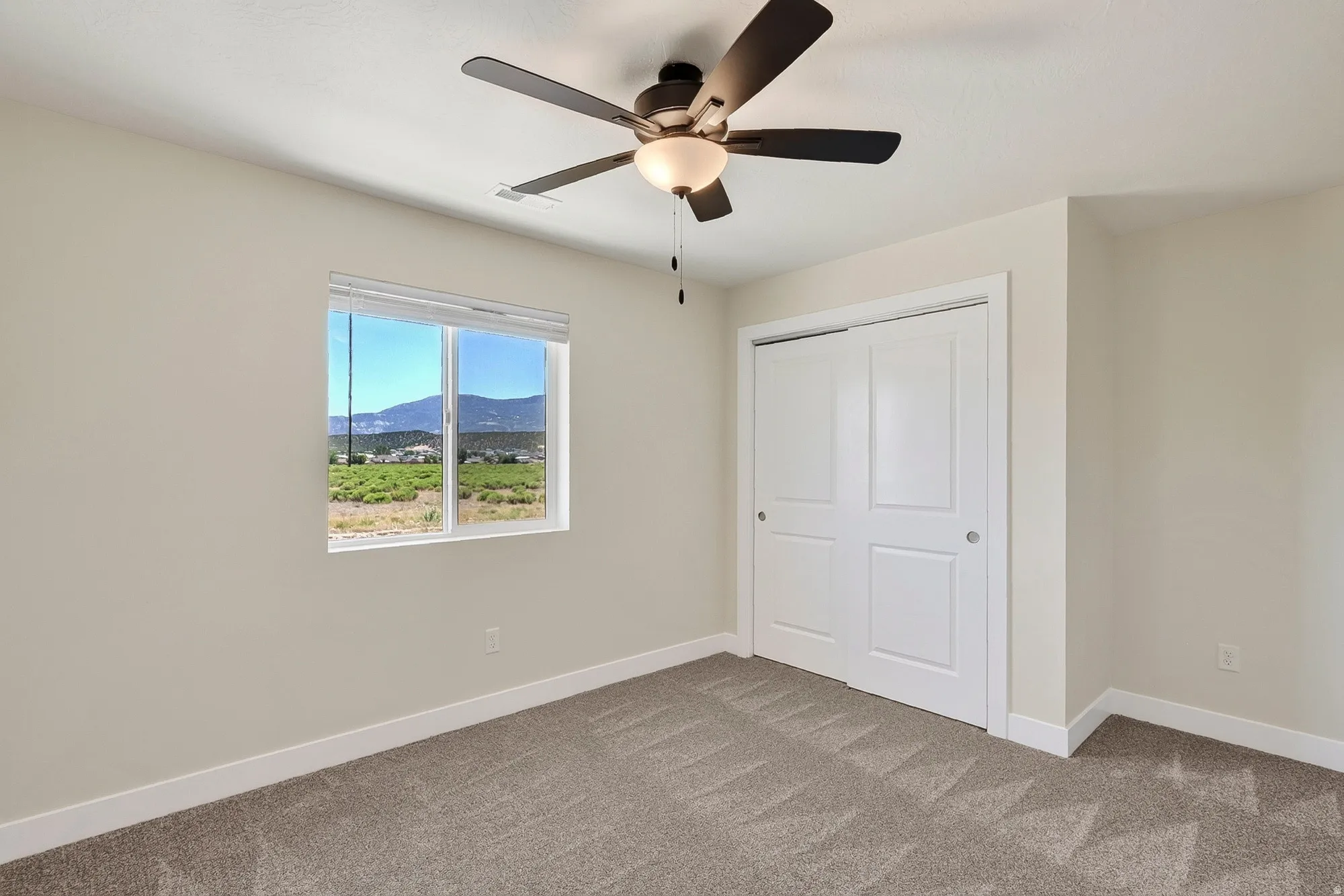 Bright bedroom featuring carpet flooring, a ceiling fan with integrated lighting, large window with mountain vistas, and white dual closet doors