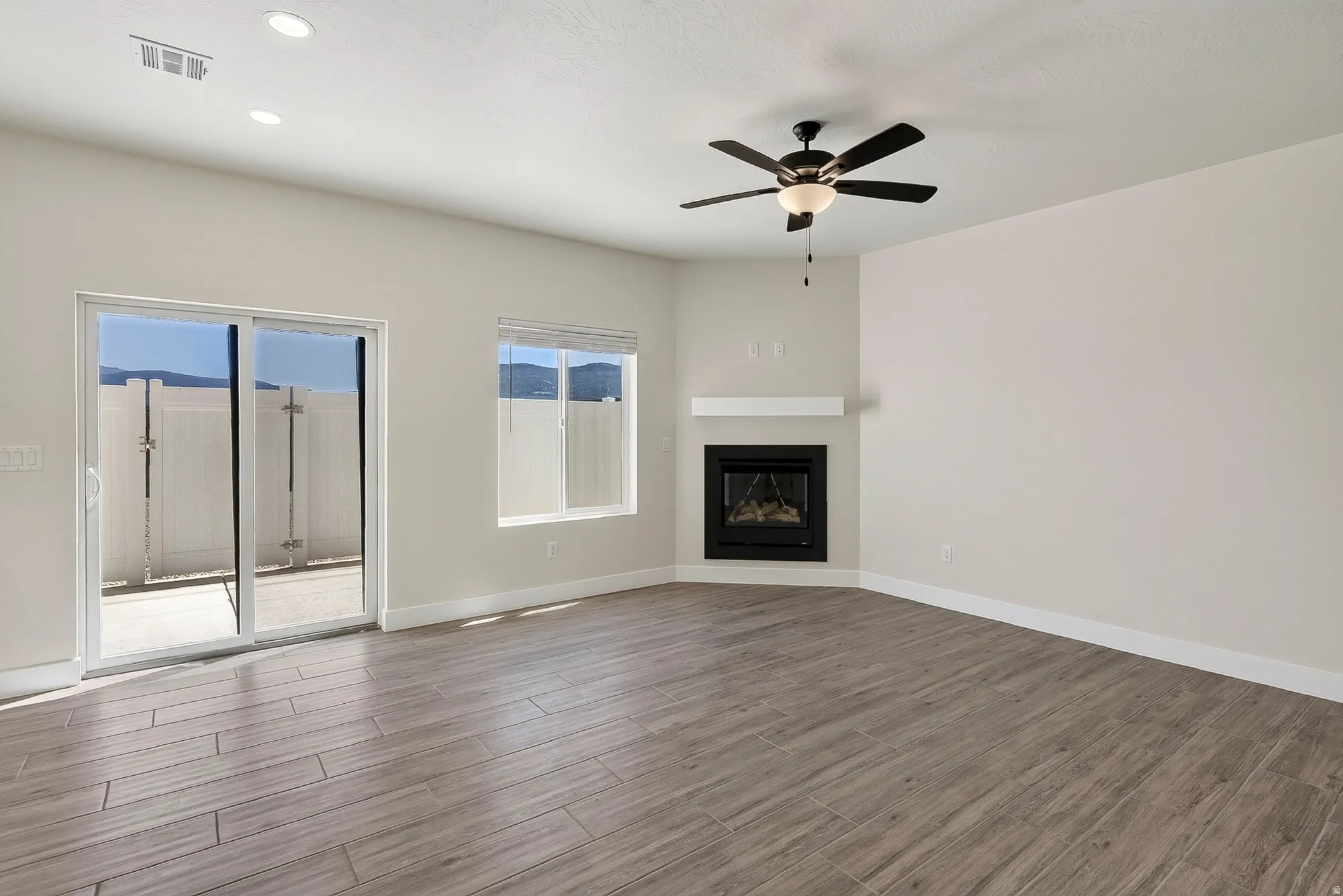 Recessed lighting, wood-finish flooring, corner fireplace with white mantel, ceiling fan with integrated lighting, and sliding glass door