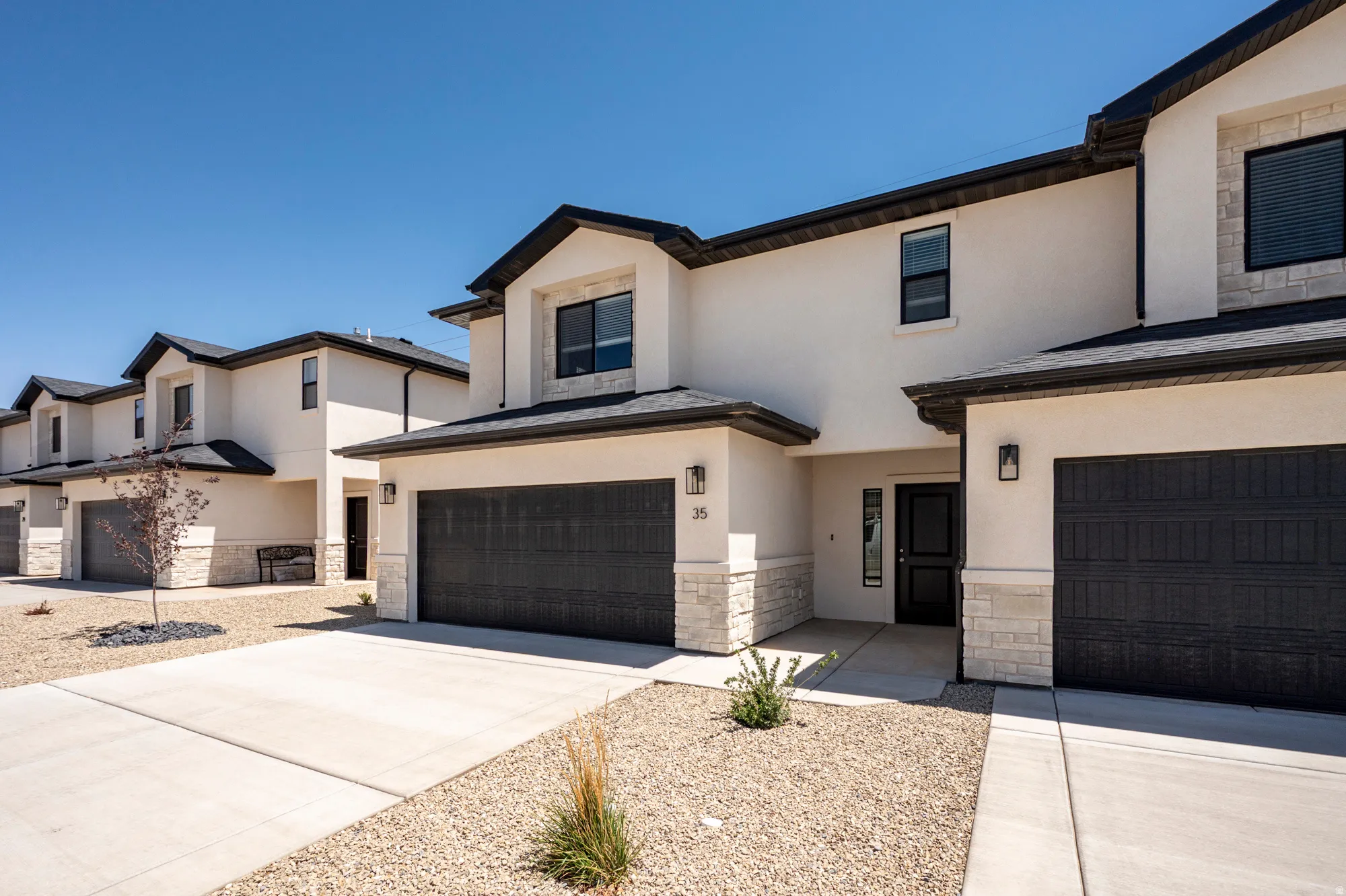 Stucco exterior with stone accents, black garage doors, paved driveways, and exterior light fixtures