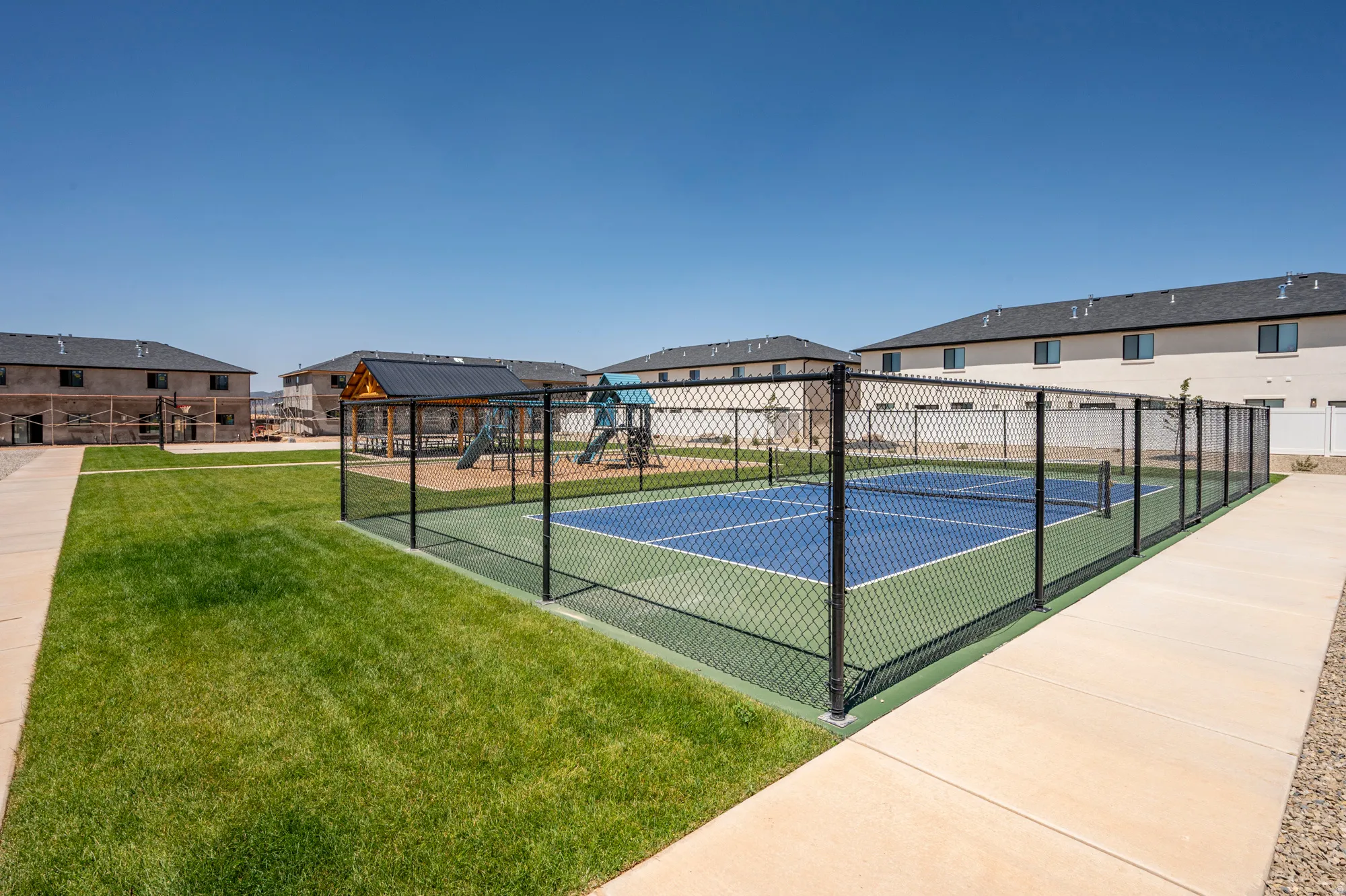 Dedicated recreational court with professional-grade playing surface enclosed by black mesh fencing, complemented by manicured lawn and concrete walkway