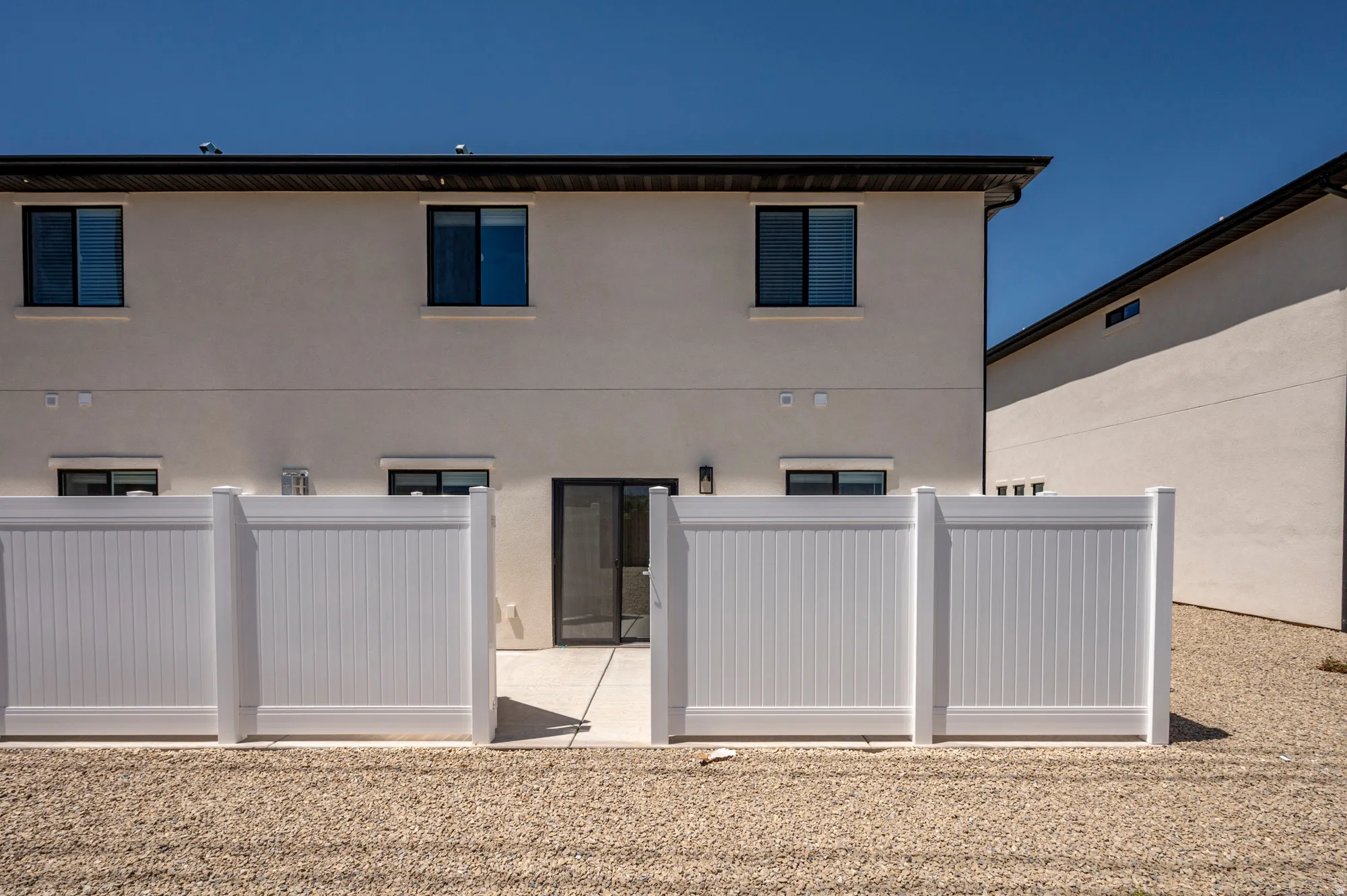 Private patio area with a sliding glass door, enclosed by a white privacy fence