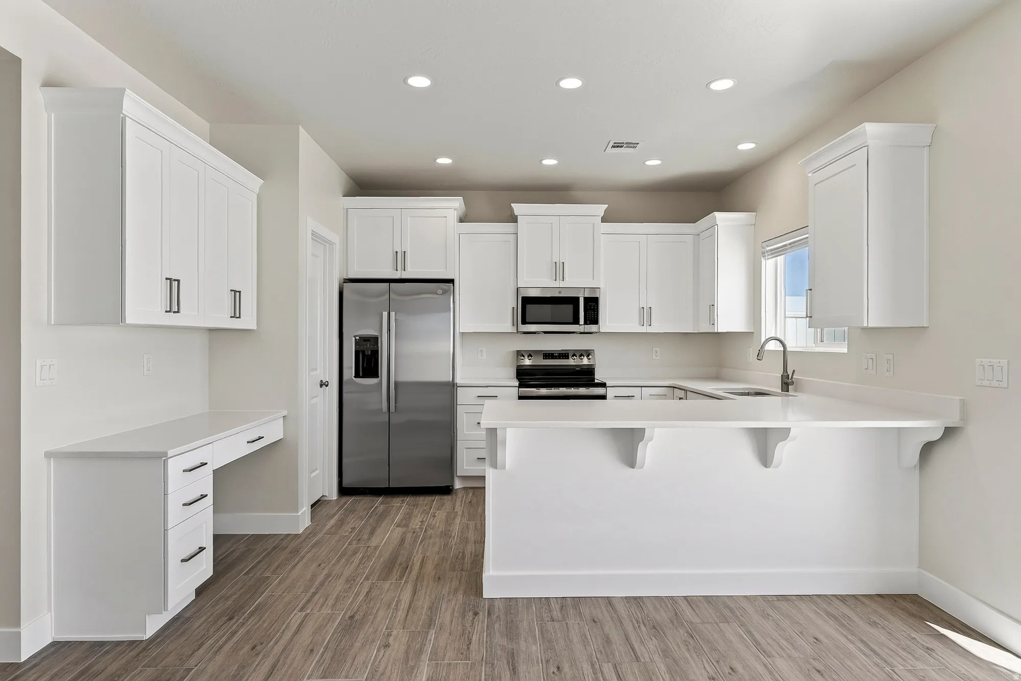 Modern kitchen featuring white cabinetry, stainless steel appliances, recessed lighting, wood-finish flooring, and a built-in desk area