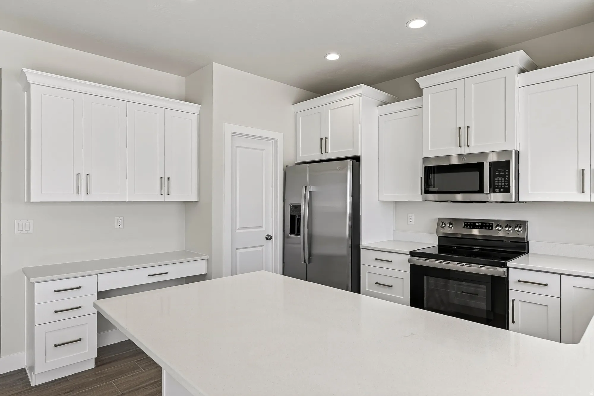 White shaker cabinetry, stainless steel appliances, light-toned countertops, and wood-finish flooring