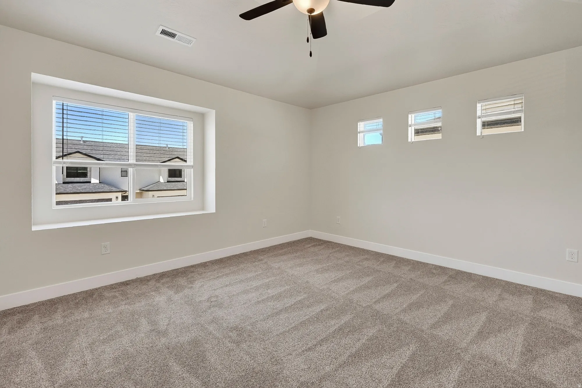 Spacious room with plush carpeting, multiple windows for natural light, and a ceiling fan