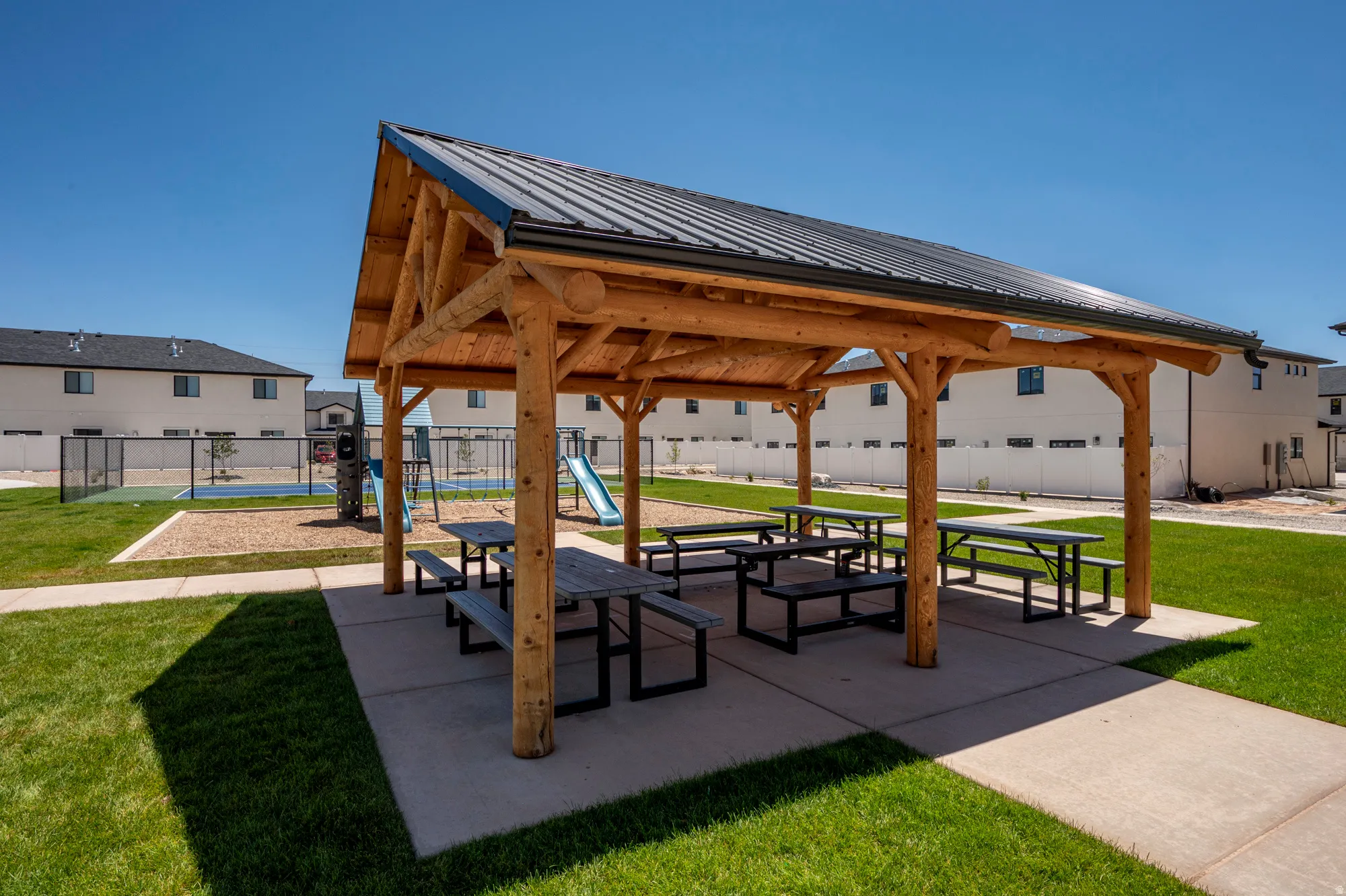 Outdoor pavilion with a metal roof, log-style columns, and multiple picnic tables