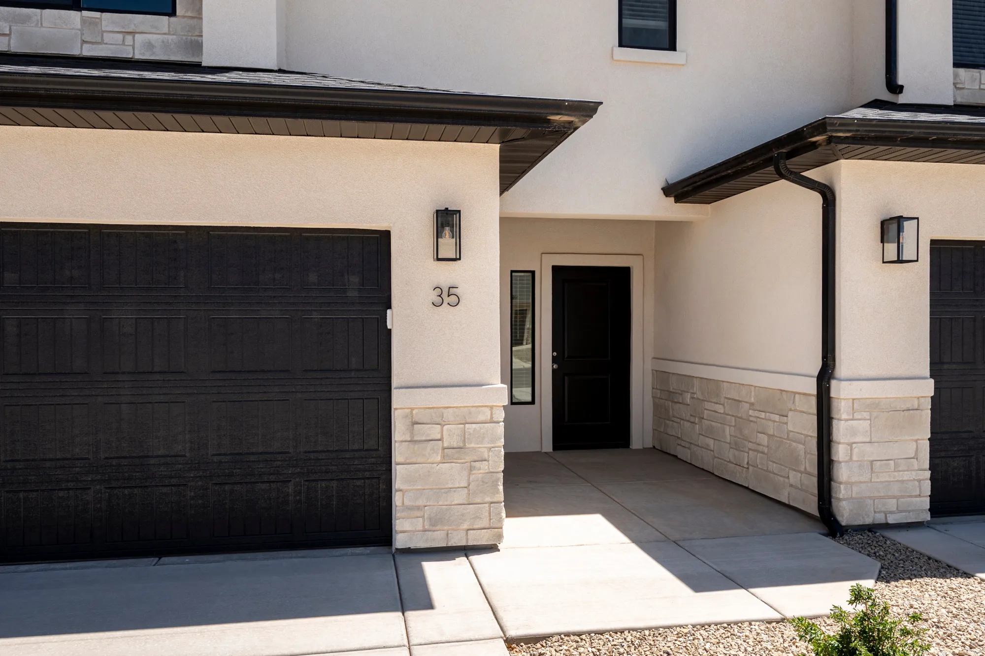Stucco exterior with stone veneer accents, black garage door, and a black entry door with a sidelight