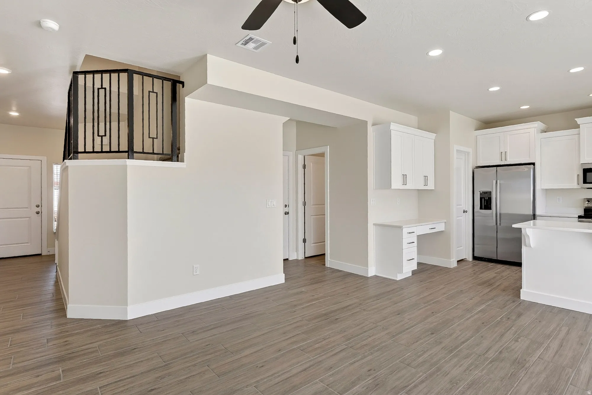 Wood-finish tile flooring throughout, white shaker cabinetry, stainless steel refrigerator, recessed lighting, and a built-in desk area