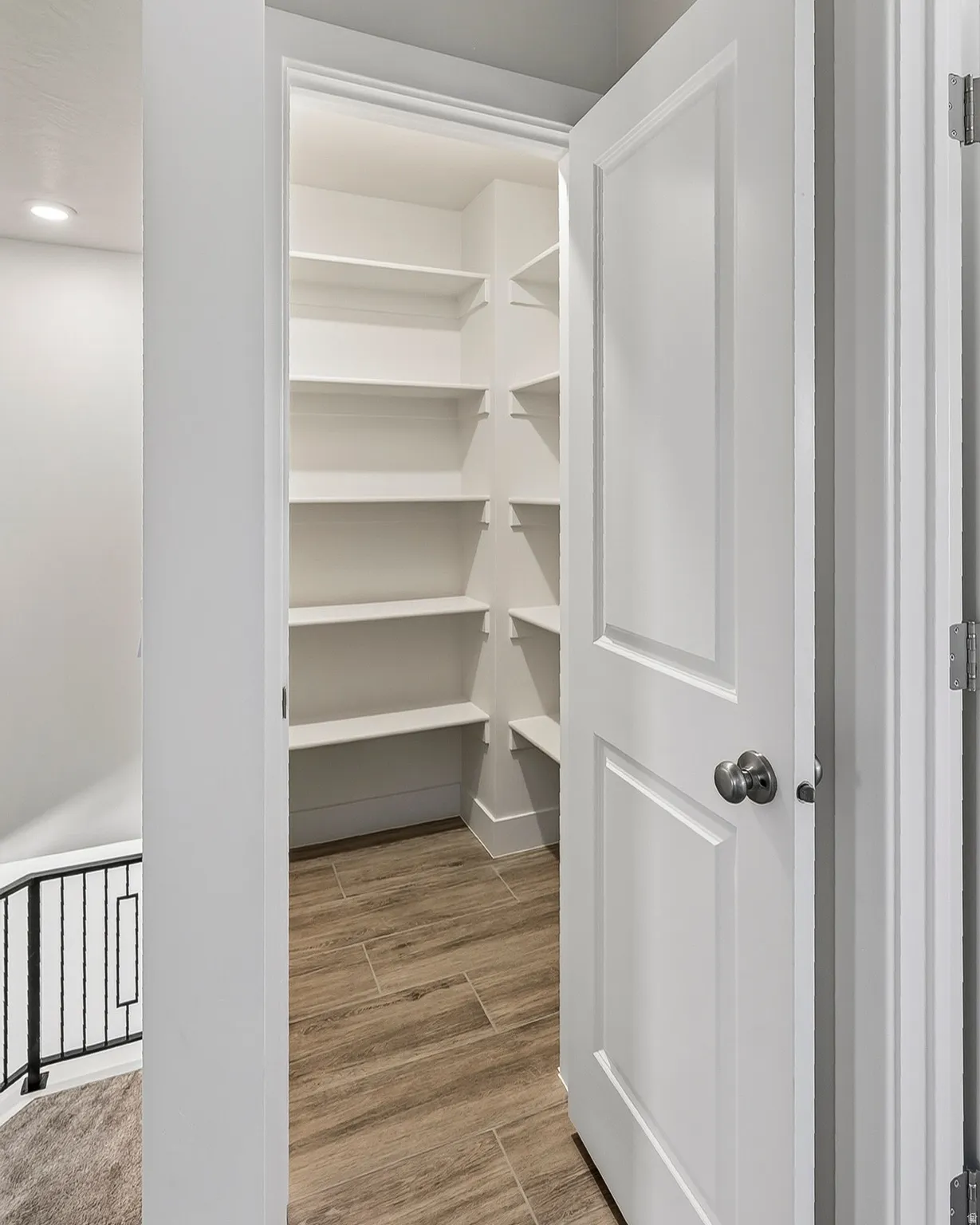 Walk-in pantry featuring extensive built-in shelving, wood-finish flooring, and a paneled door with brushed nickel hardware