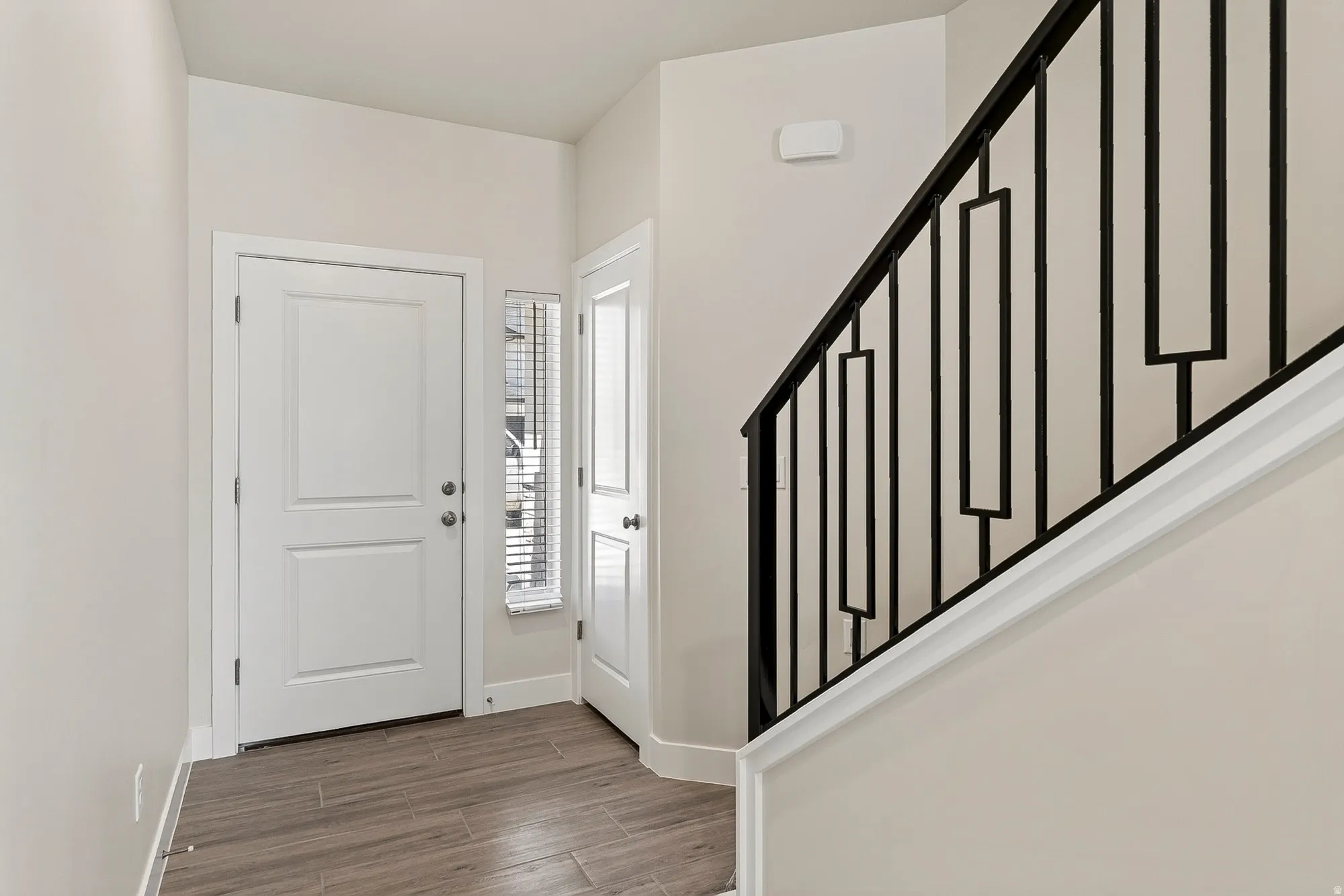 Wood-finish flooring, white panel doors, and a staircase with a black metal railing