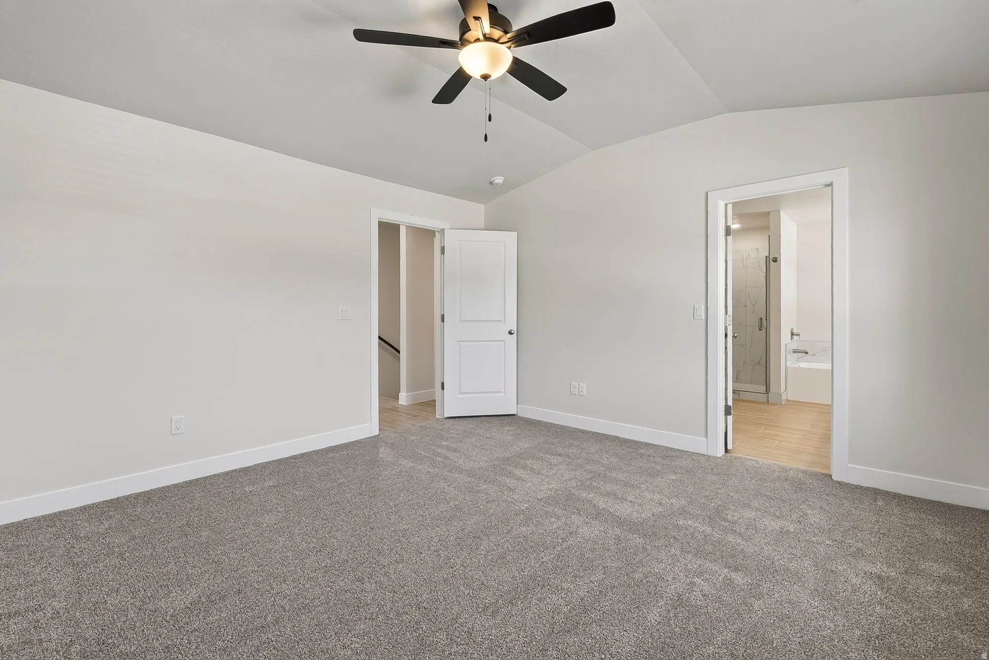 Vaulted ceilings with a ceiling fan, plush gray carpeting, and a white paneled door