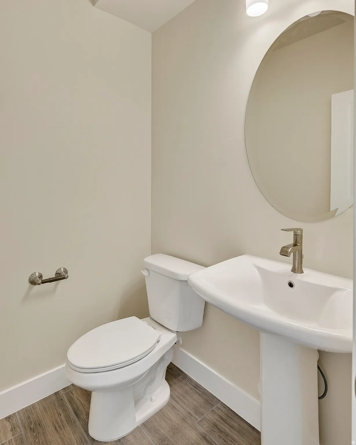 Pedestal sink with a brushed nickel faucet, an oval mirror, and wood-finish flooring