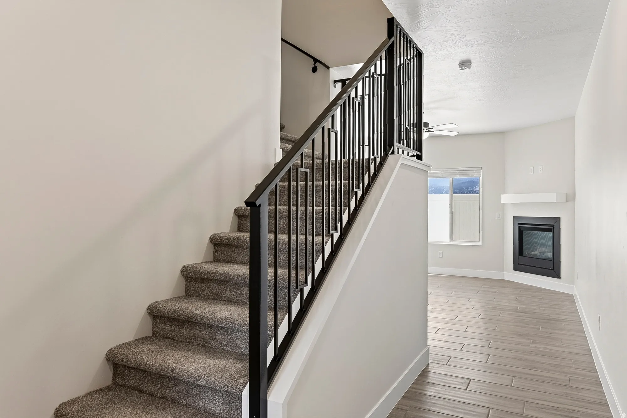 Carpeted staircase with black metal balusters, plank-style flooring, a white mantel, and a built-in fireplace