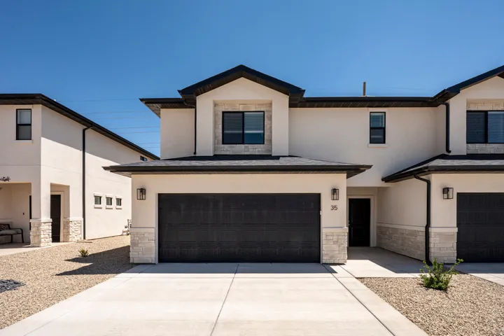 Stucco exterior with stone accents, black-framed windows, a dark garage door, and modern exterior lighting fixtures