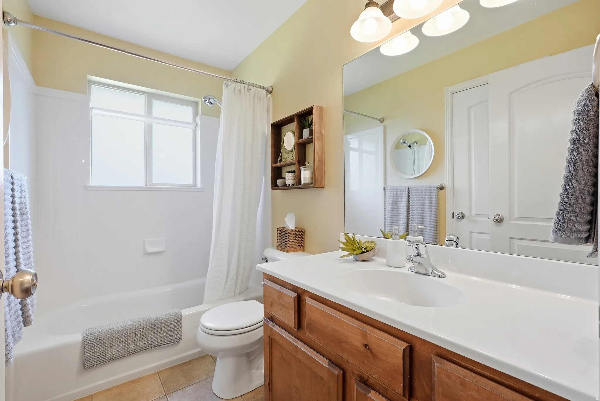 Bathroom featuring a tub/shower combination, window with privacy covering, single vanity with a white countertop and integrated sink, and wood-finish cabinetry