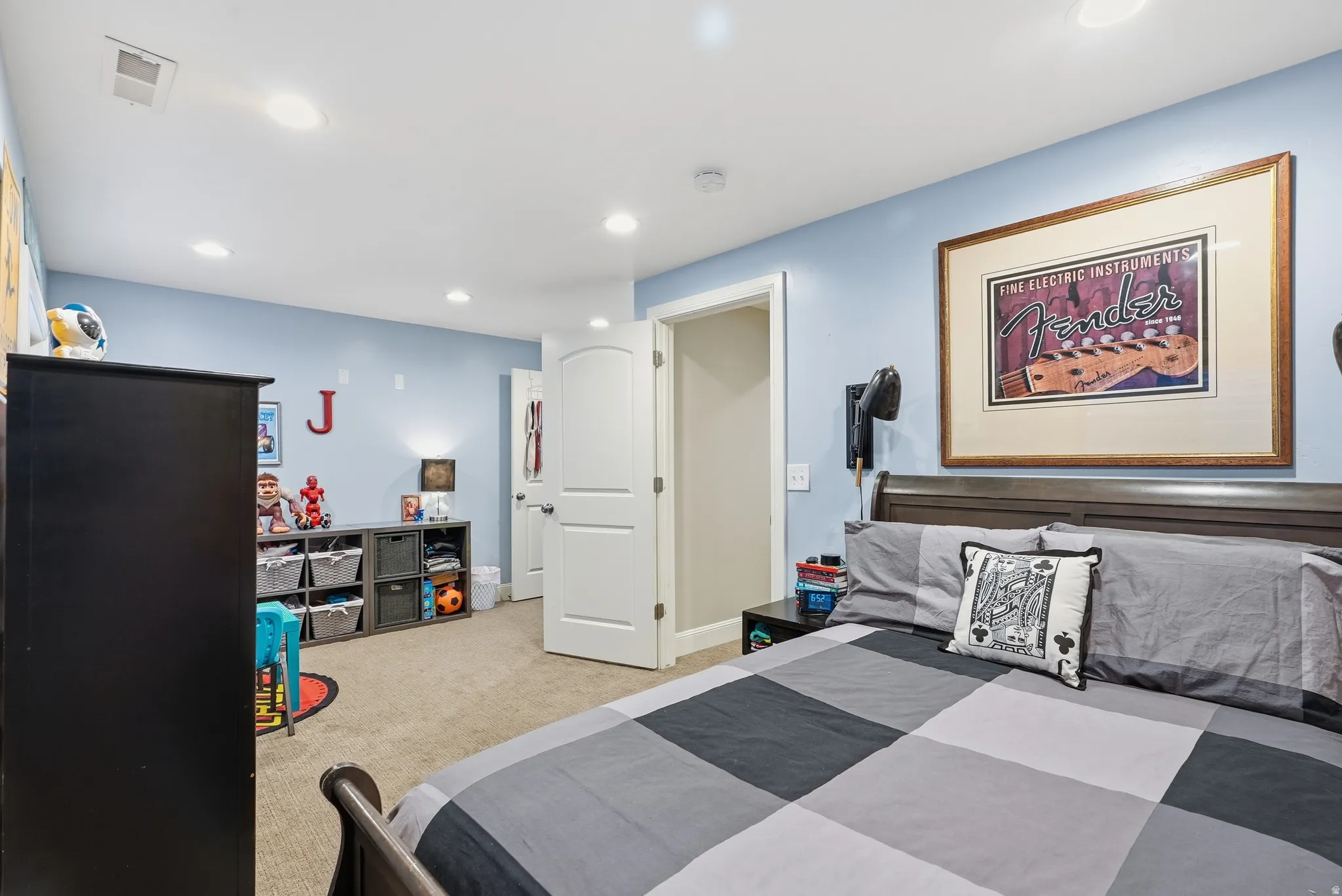 Recessed lighting, wood-finish bed frame, light blue walls, and white interior door