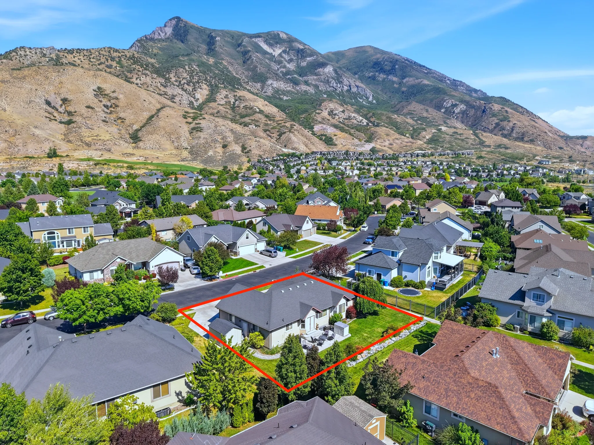 Aerial perspective highlighting a residential property with a stone retaining wall, mature trees, and an exterior patio with paved surfaces
