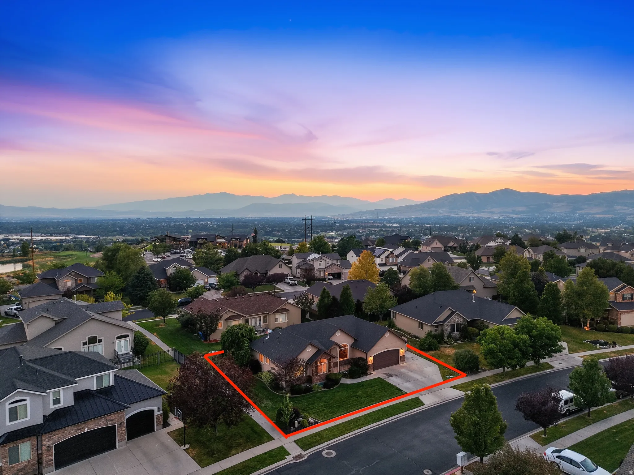 Stunning aerial perspective showcasing this brick residence situated on an expansive corner lot with mature landscaping, manicured lawn, and mountain vistas in the distance