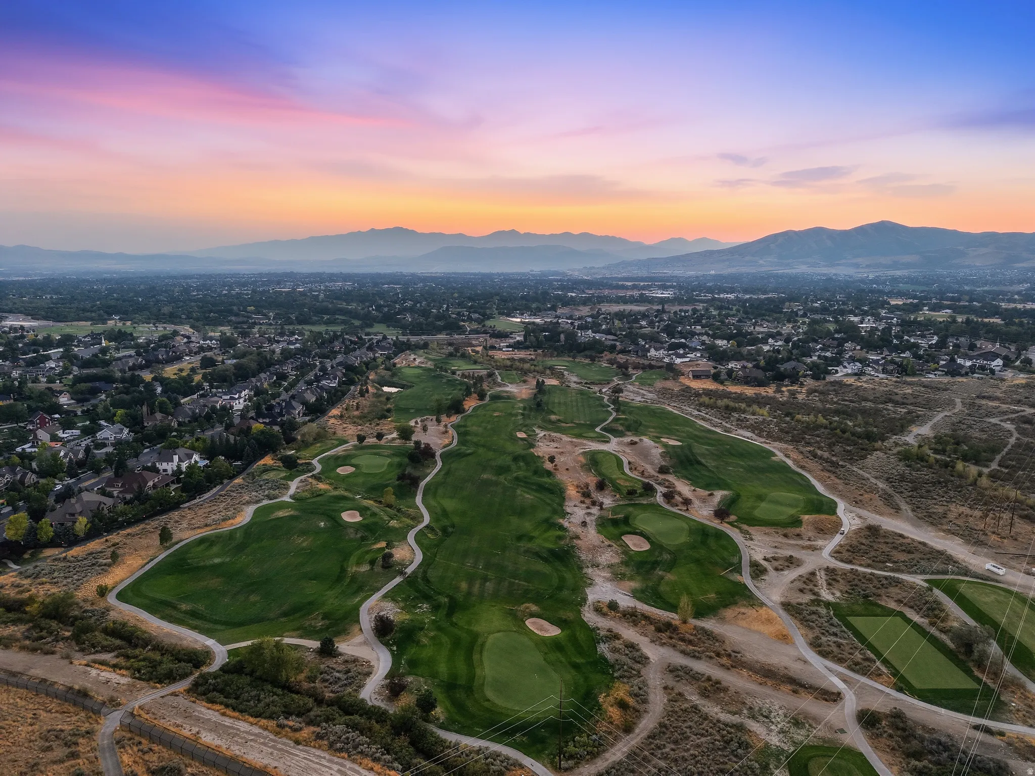 Expansive golf course with manicured greens and walking paths, surrounded by residential properties and distant mountains