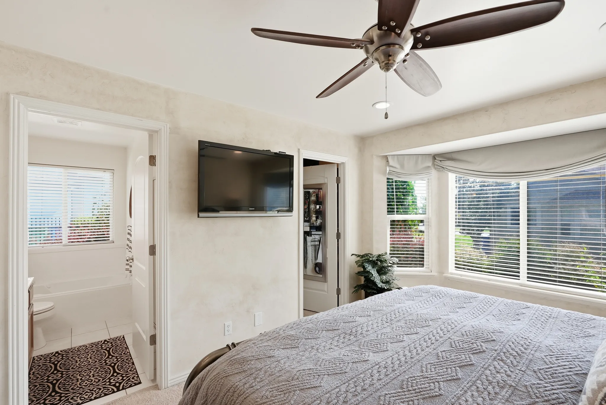 Recessed lighting, ceiling fan with light fixture, bay windows with blinds, and an attached bathroom with a window